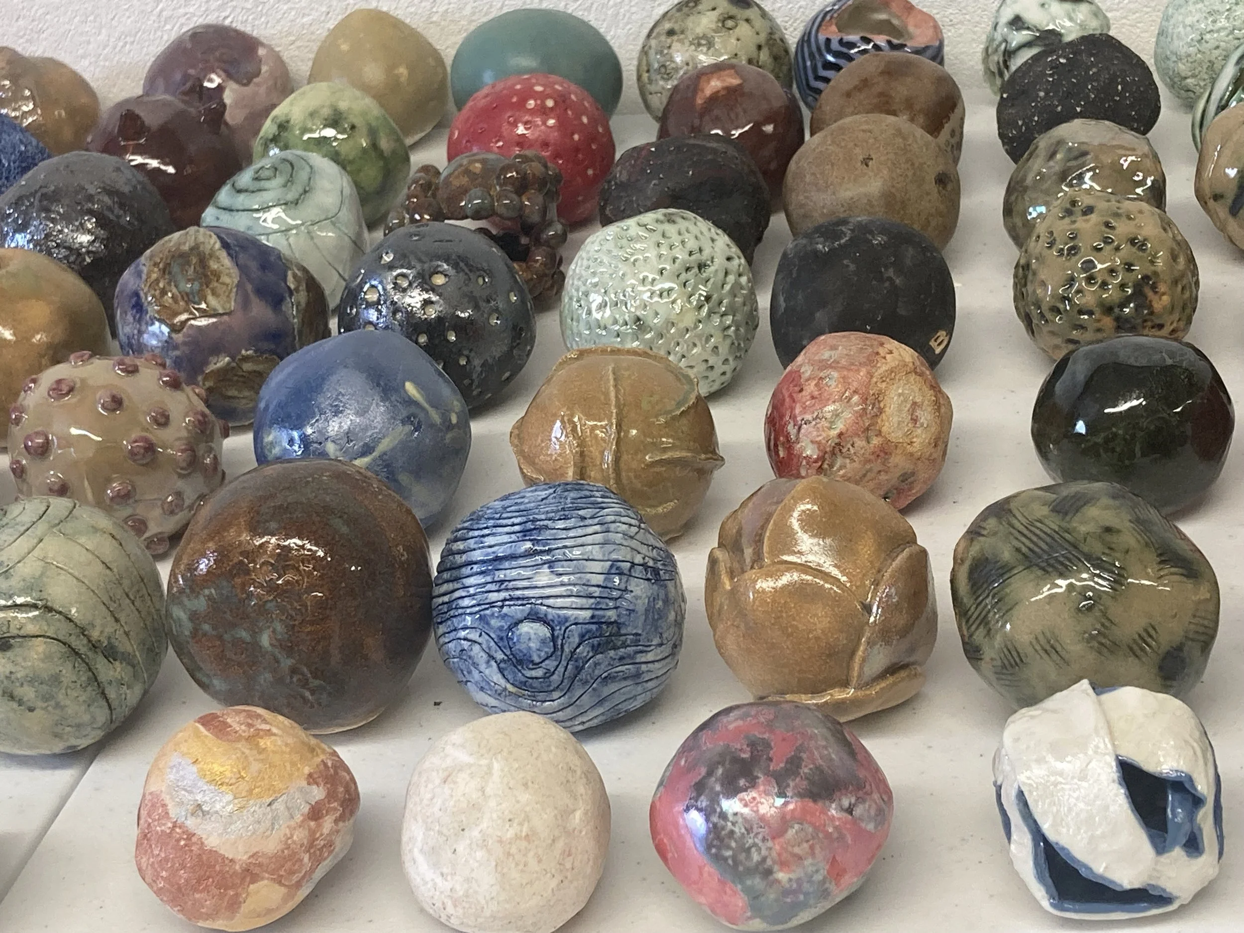 A collection of various decorative marbles made from glass and stone, displaying different colors, textures, and patterns, arranged on a white surface.