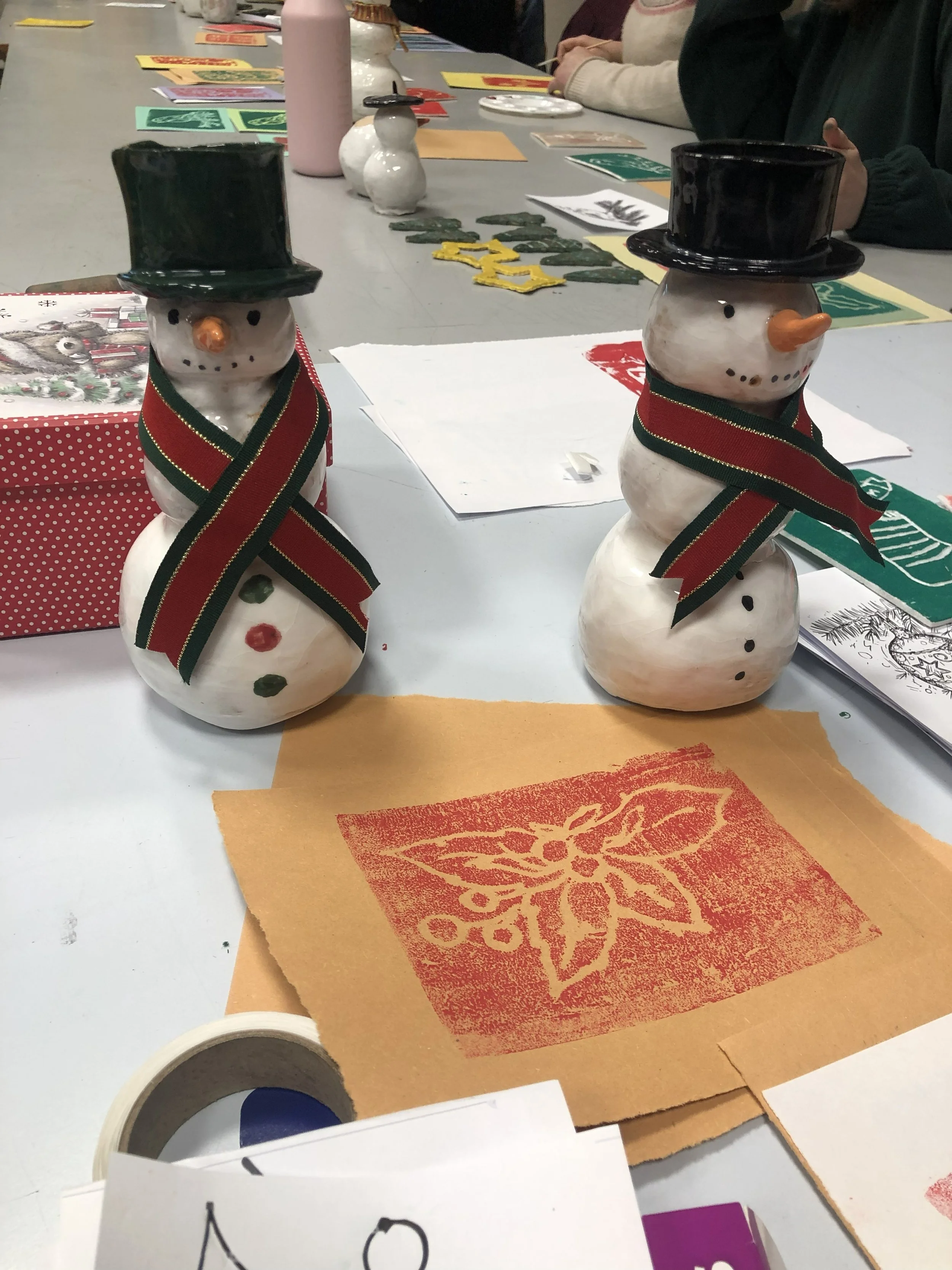 photo of ceramic snowmen and lino prints of hollies on a festive craft workbench