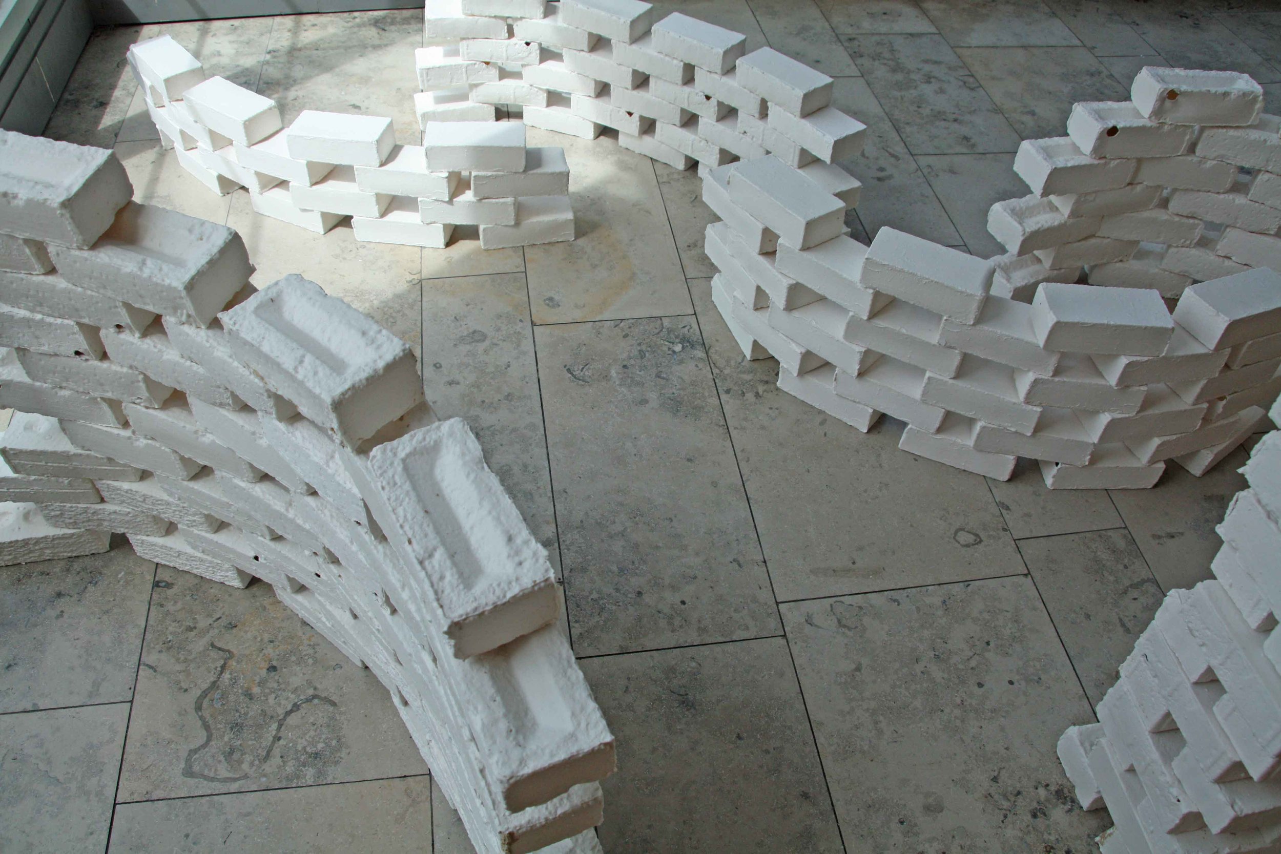 Stacks of white bricks arranged in curved formations on a tiled floor.