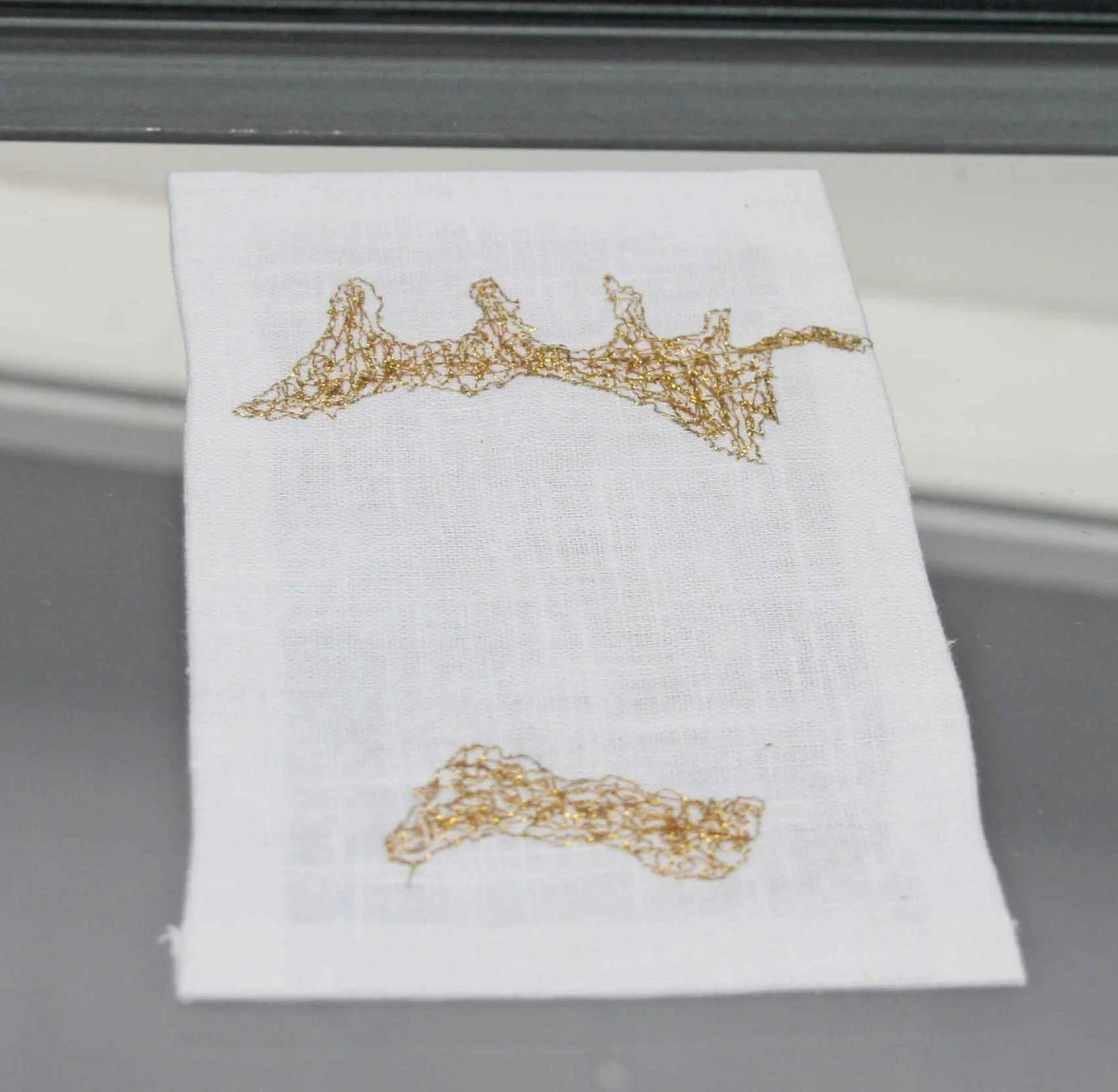 Close-up of a piece of white textile with gold thread embroidery in a delicate, abstract pattern.