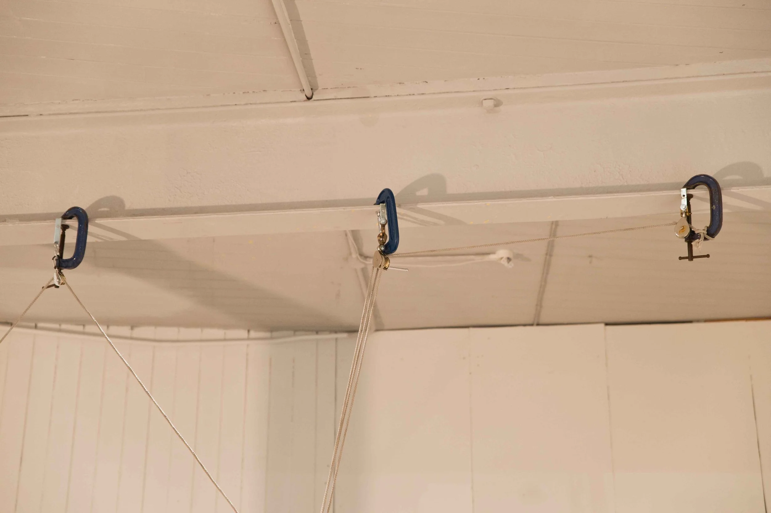 Ceiling with three clamps attached to strings hanging downward, possibly for painting or hanging objects.