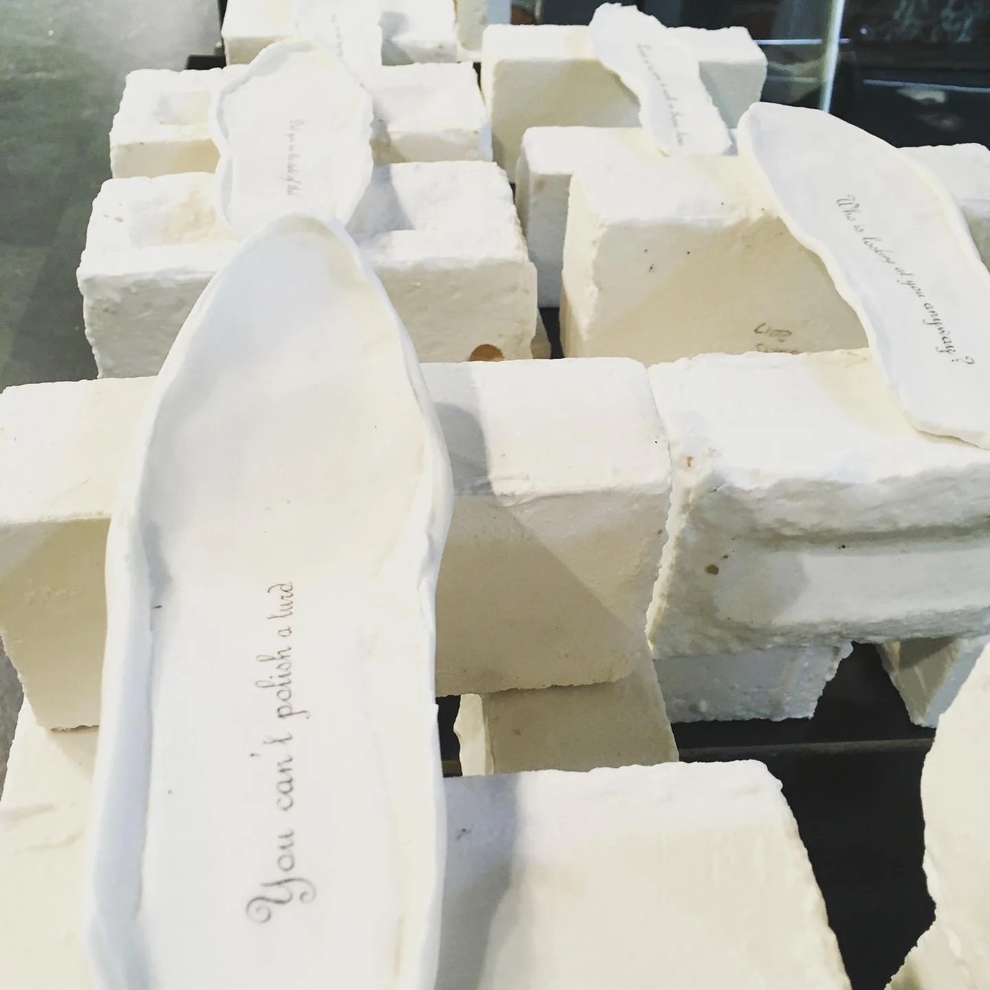 Close-up of white porcelain bricks and footprints with handwritten labels, stacked together on a dark surface.