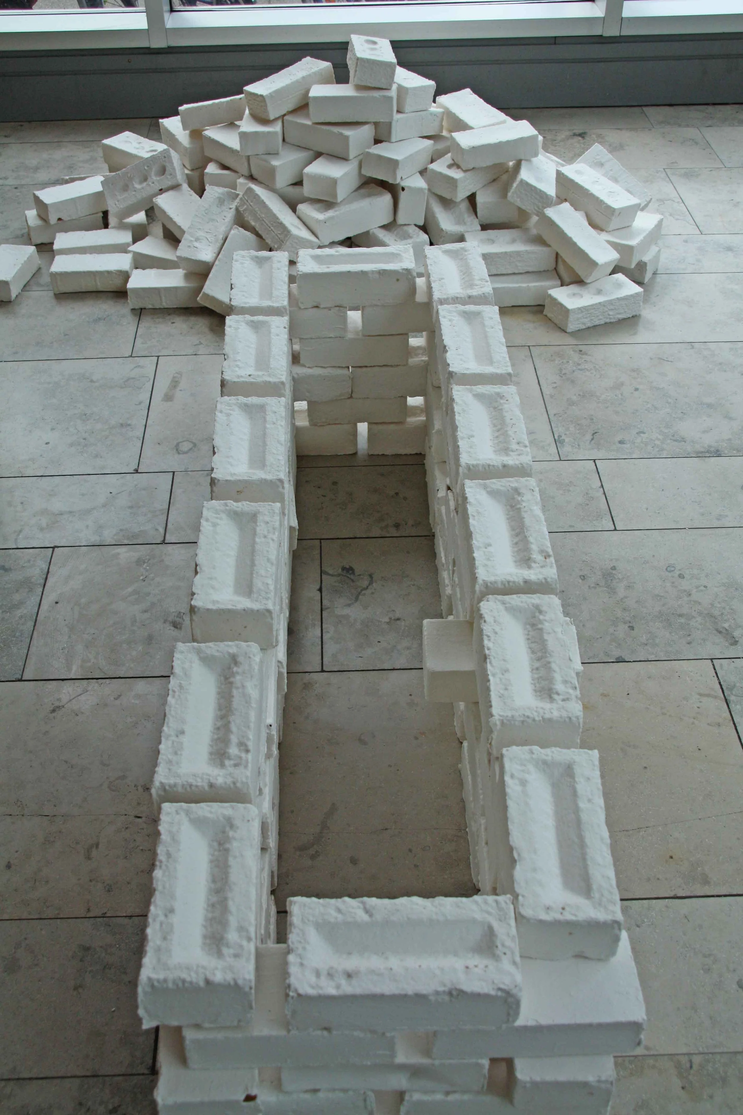 Stack of white bricks arranged in a structure on a tiled floor, with additional bricks scattered around.
