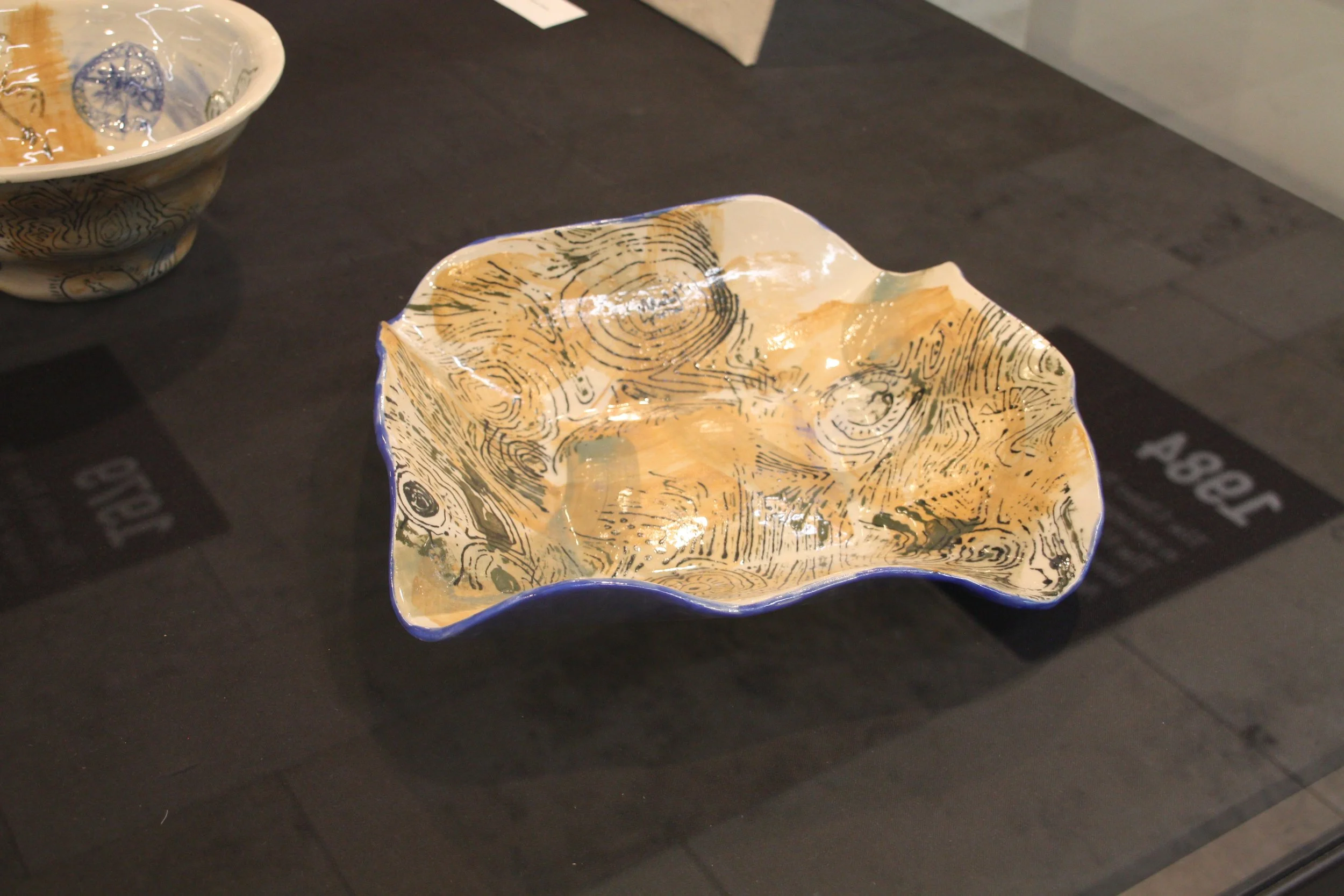 A decorative ceramic bowl with a wavy, scalloped edge and a design resembling wood grain and geographic lines inside.