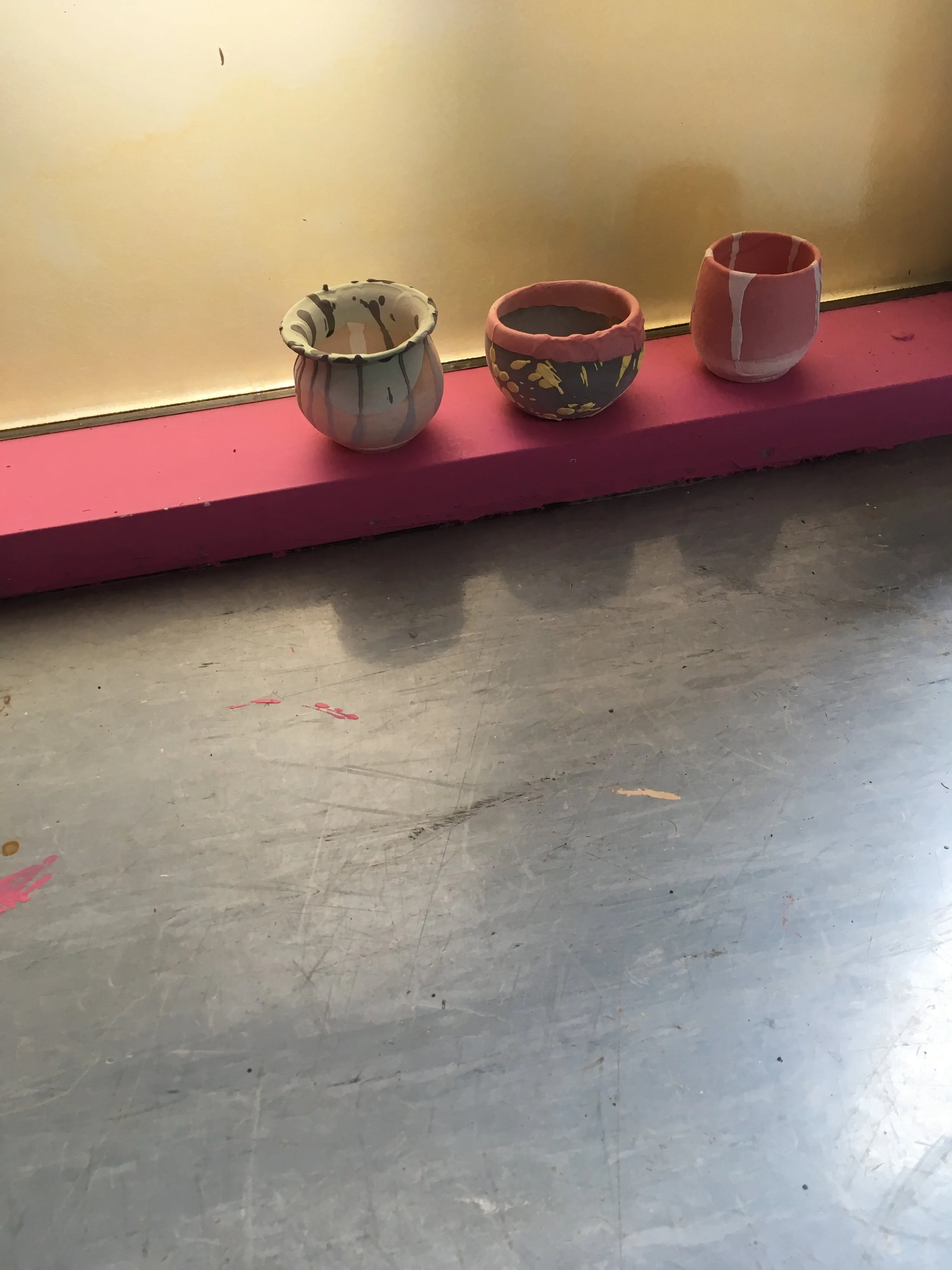 Three small decorative pots with various patterns placed on a pink ledge against a beige wall.