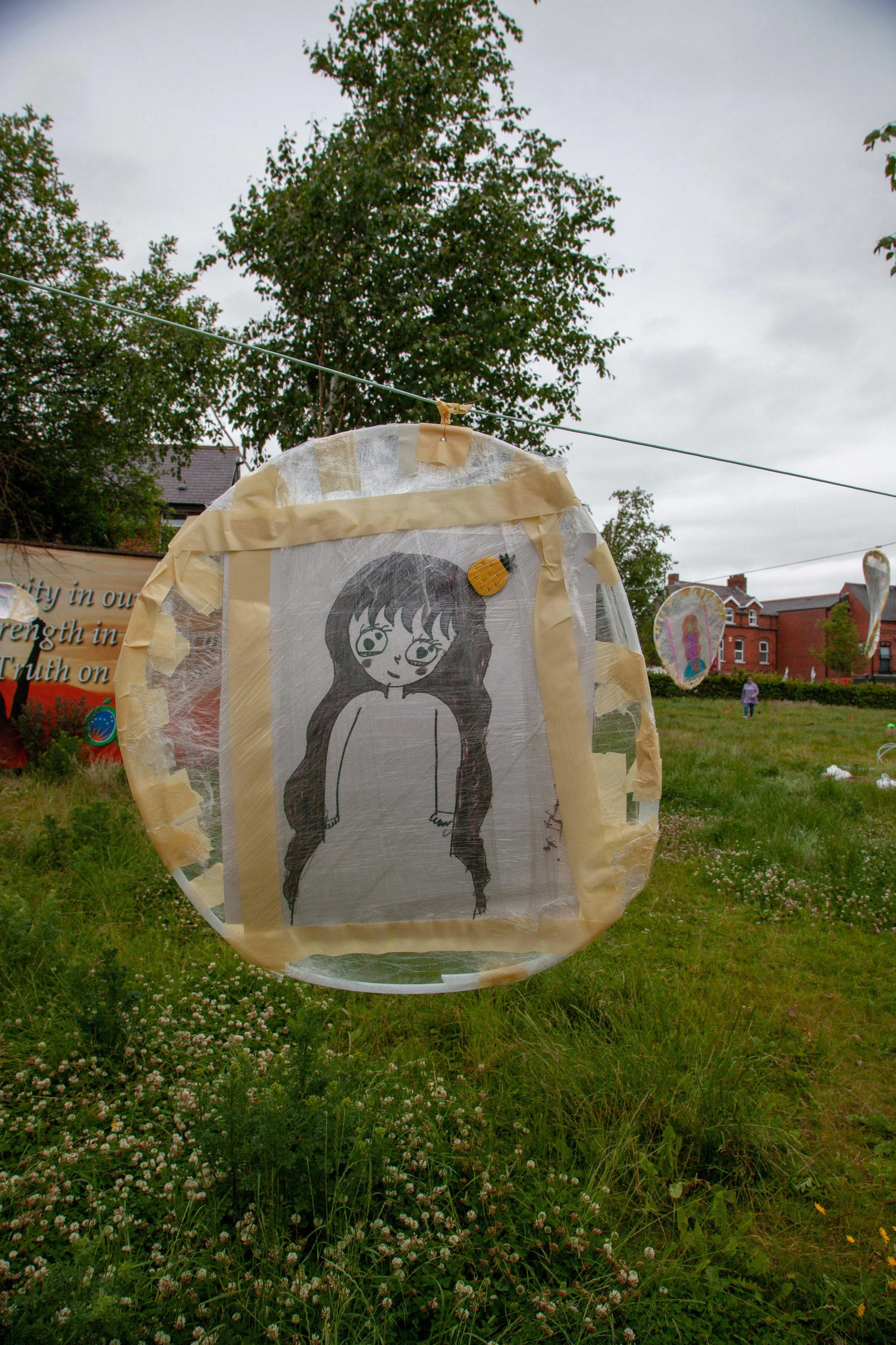 Hoop with a black and white illustration of a girl with long hair, set outdoors on a grassy area with trees, buildings, and other lanterns in the background under a cloudy sky.