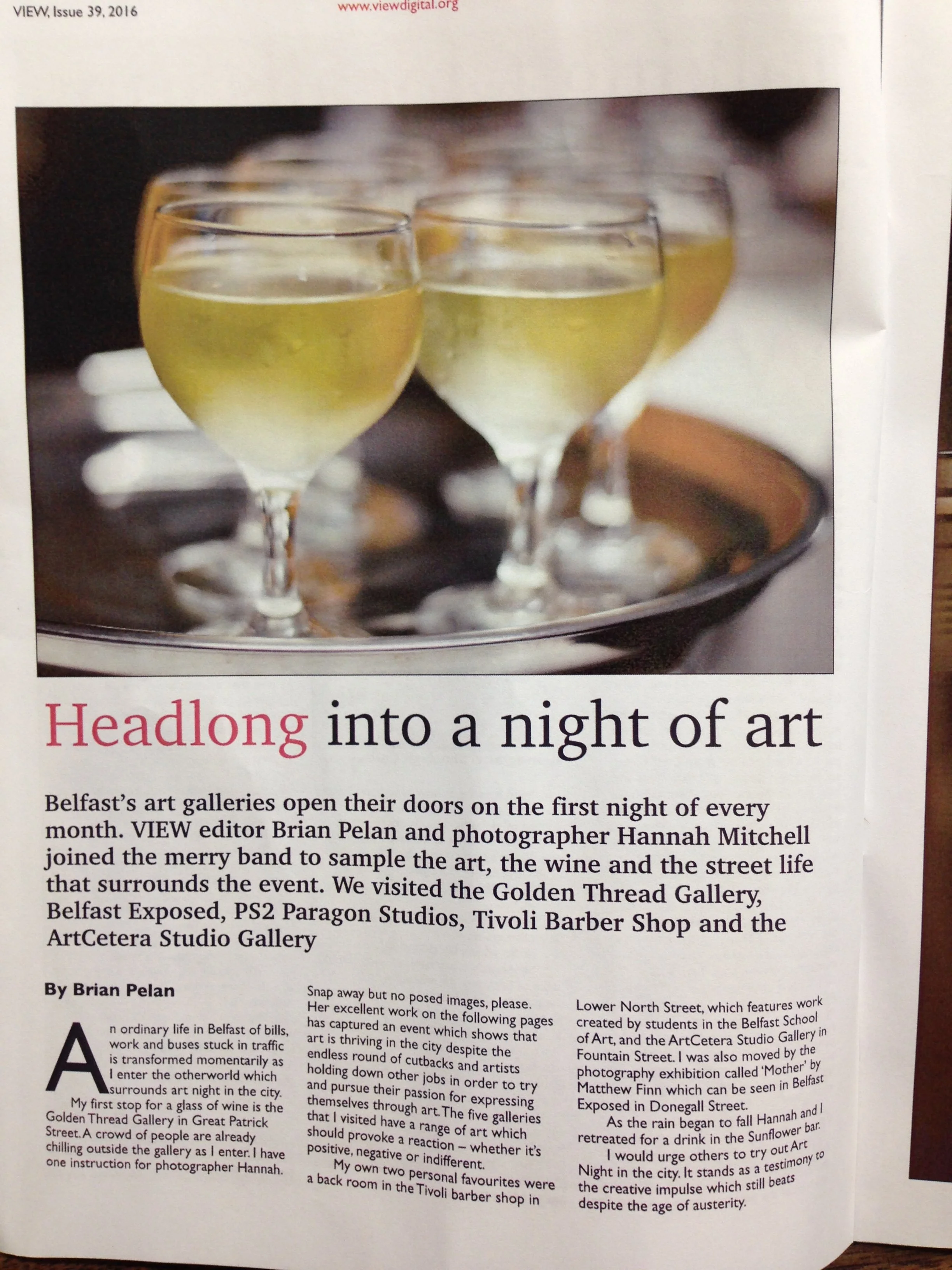 Close-up of a newspaper page showing a photograph of four glasses of white wine on a silver tray, with part of the headline reading "Headlong into a night of art" and a paragraph of text underneath.