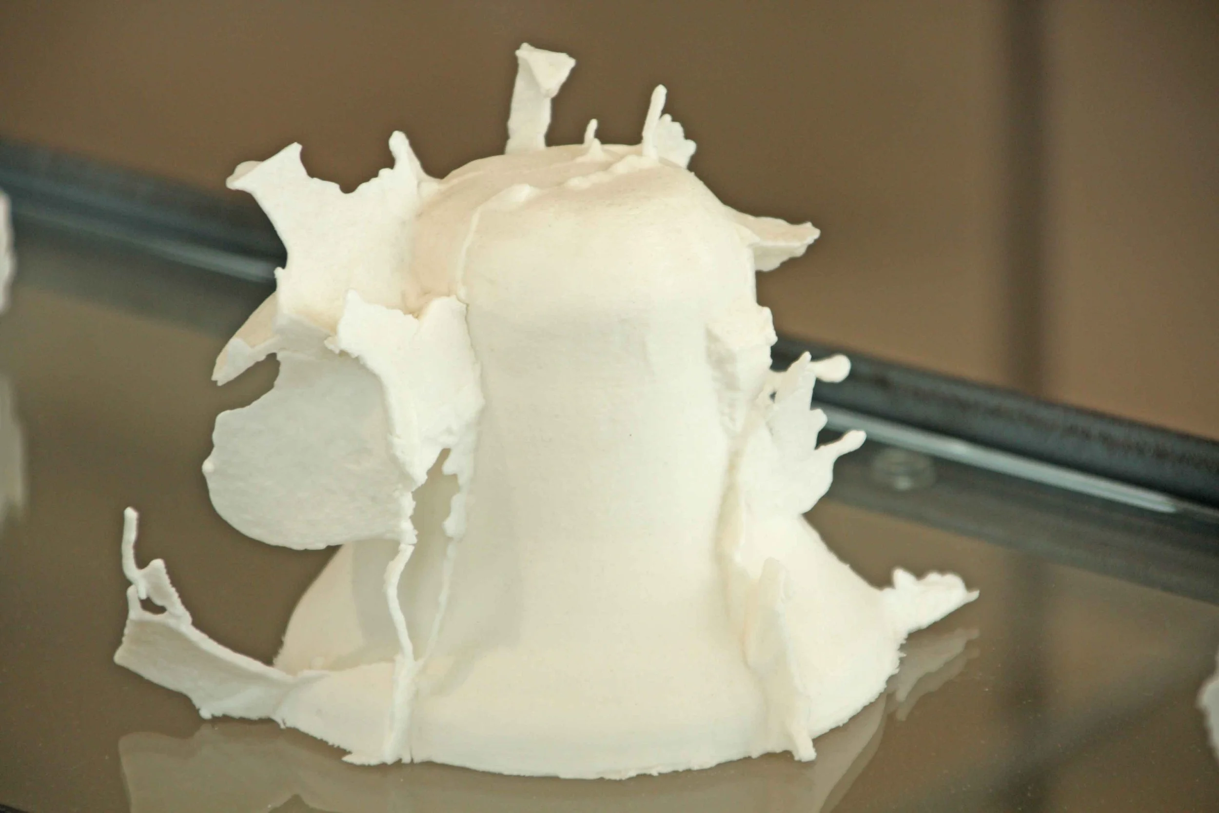 Close-up of a white bell resembling a complex, abstract sculpture with irregular edges, set on a flat surface.