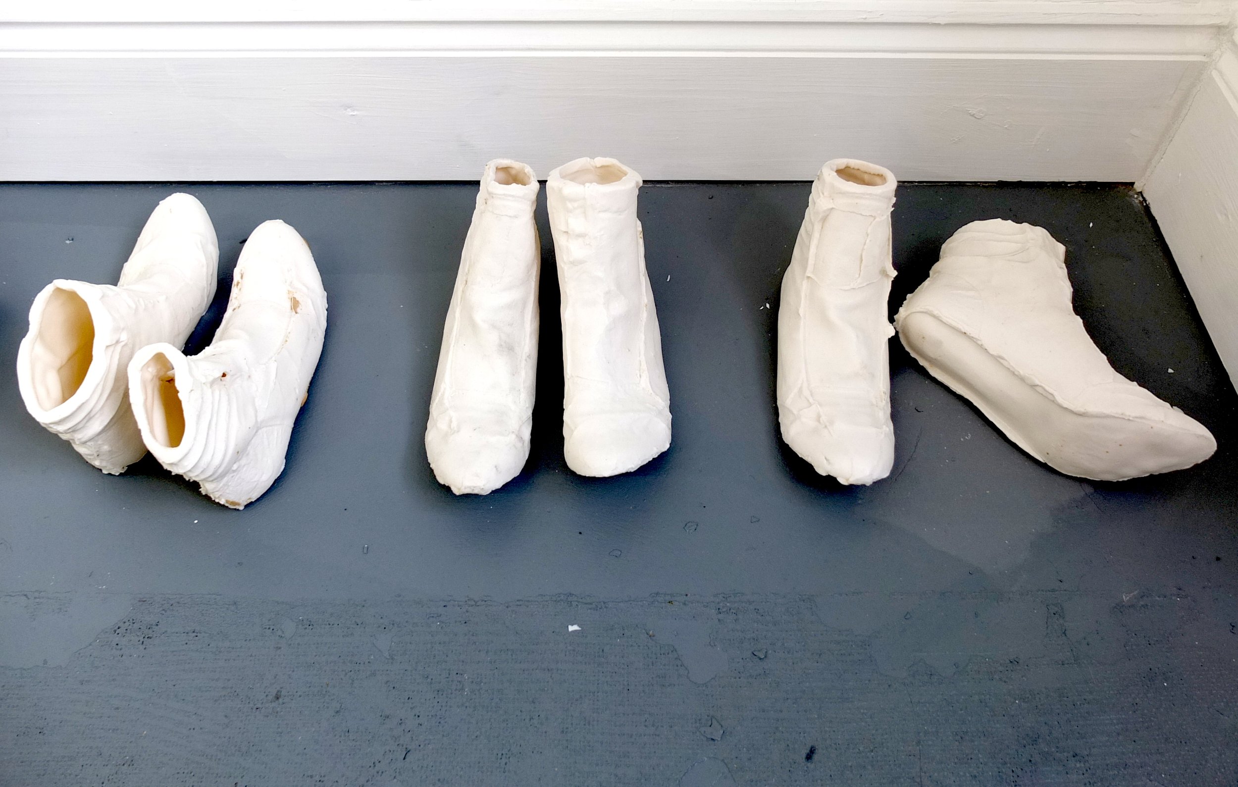 Collection of white ceramic boots and shoes displayed on a dark gray surface