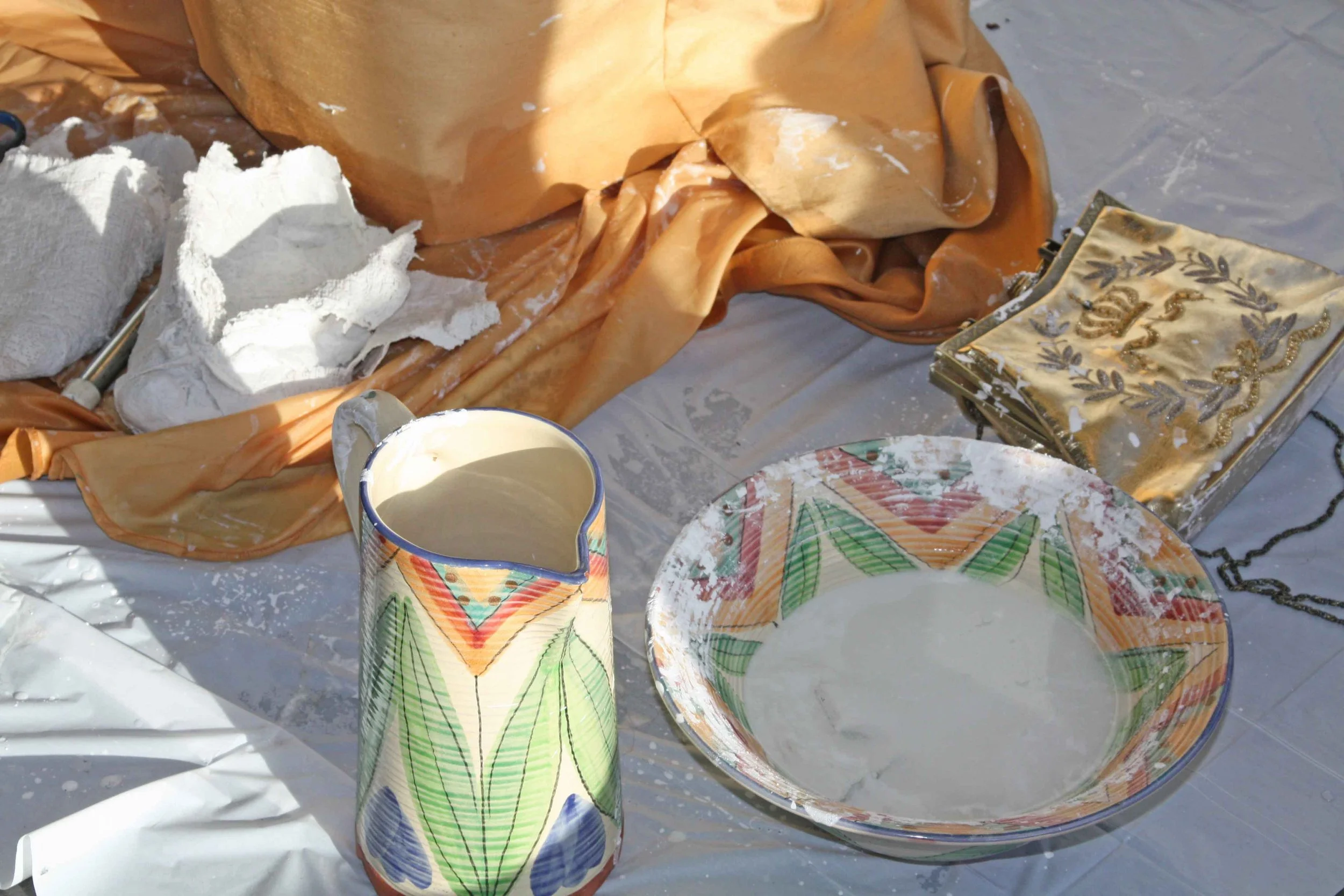 Broken ceramic cups and plates with colorful patterns, some containing white powder, placed on aluminum foil, possibly in a kitchen or workshop setting.