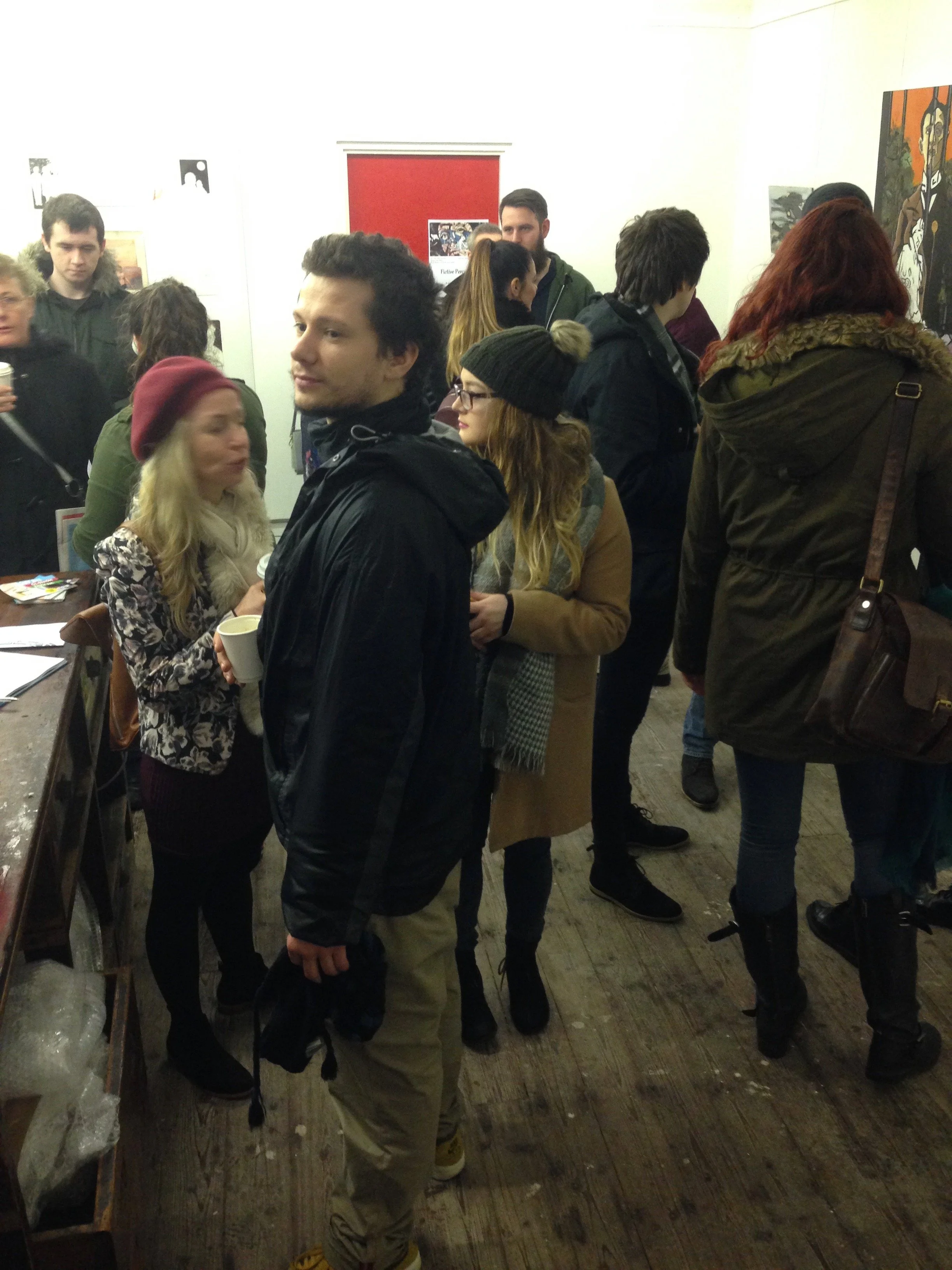 A group of people gathering in an art gallery, looking at artwork and engaging in conversations.