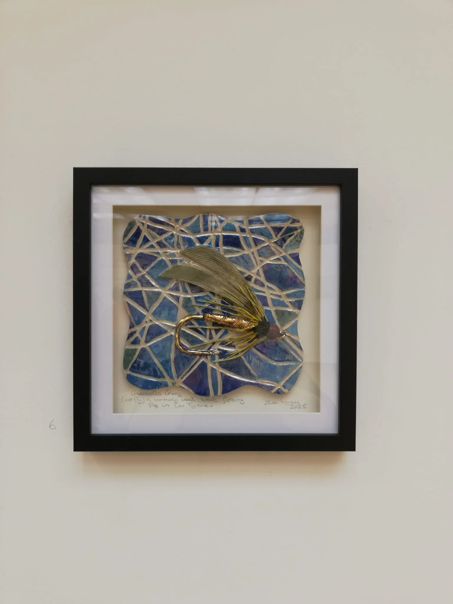Framed artwork of a fly with golden wings and a stained glass background, with handwritten note beneath it.