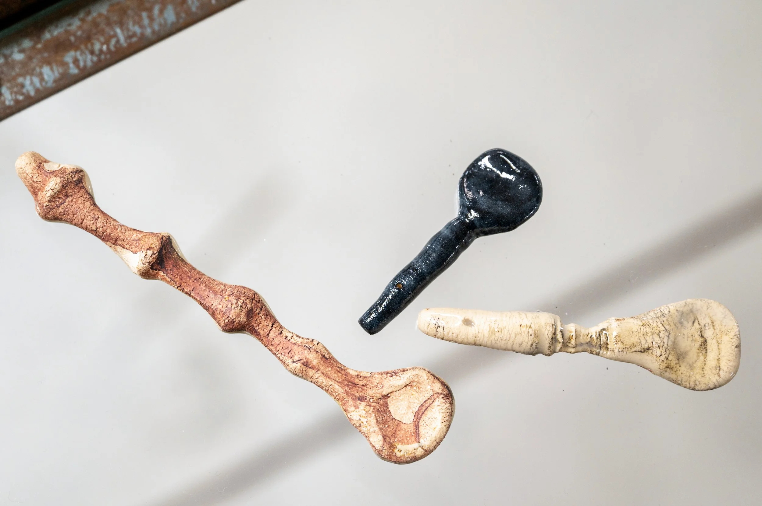 Close-up of several violin tuning pegs made of different materials and colors, arranged in a row on a white surface.