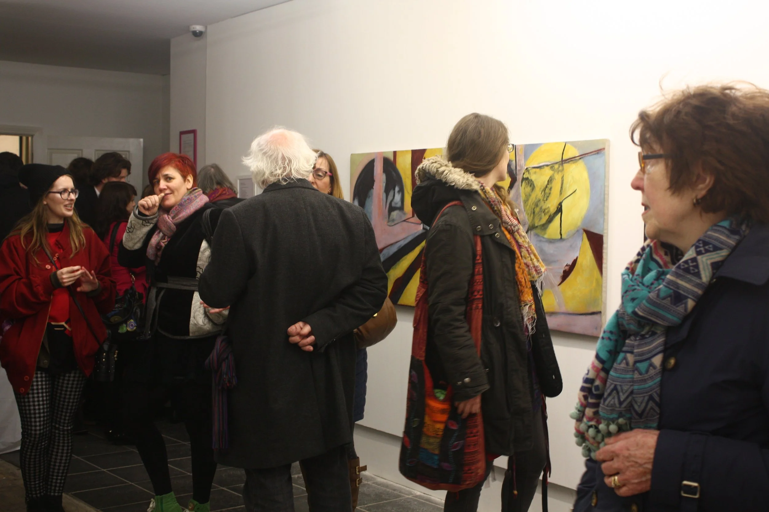 A group of people at an art gallery viewing colorful paintings on the wall.