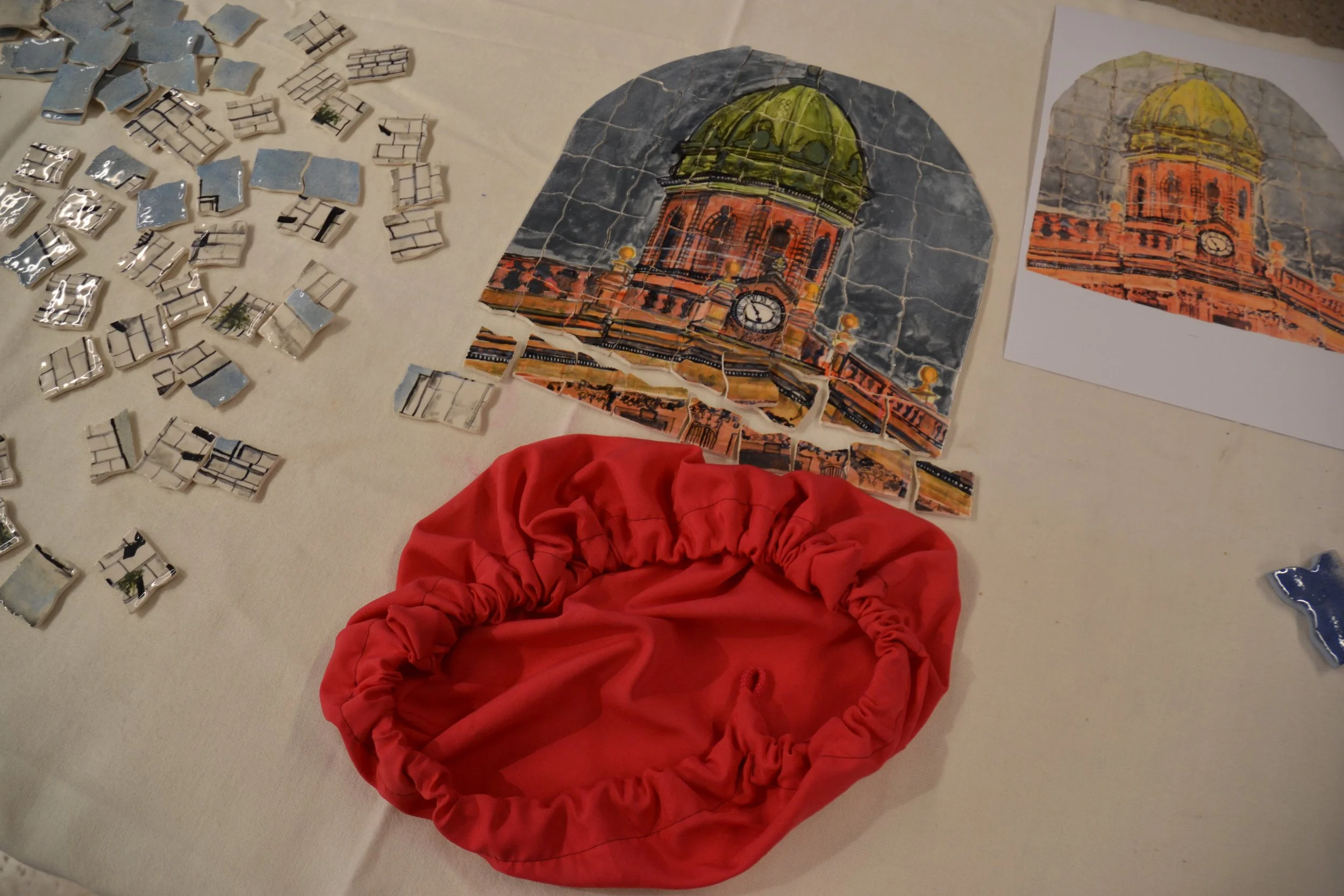 A partially completed jigsaw puzzle of a clock tower with a green dome and orange brick structure, surrounded by puzzle pieces and a printed reference image on paper, all on a white surface.