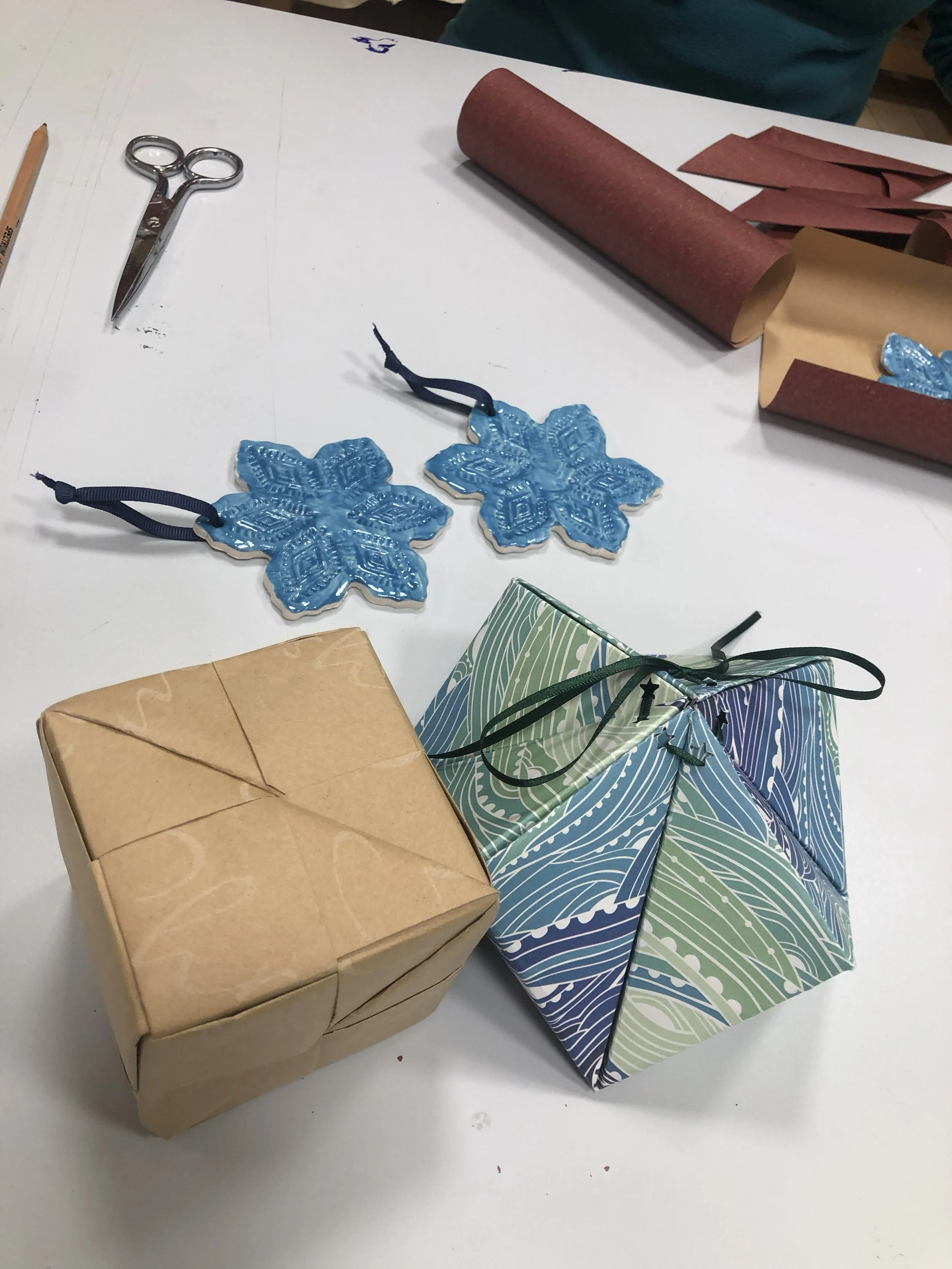 art table with scissors, squares of paper, start shaped ceramic tree decorations a cube shaped paper origami box and diamond shaped origami box