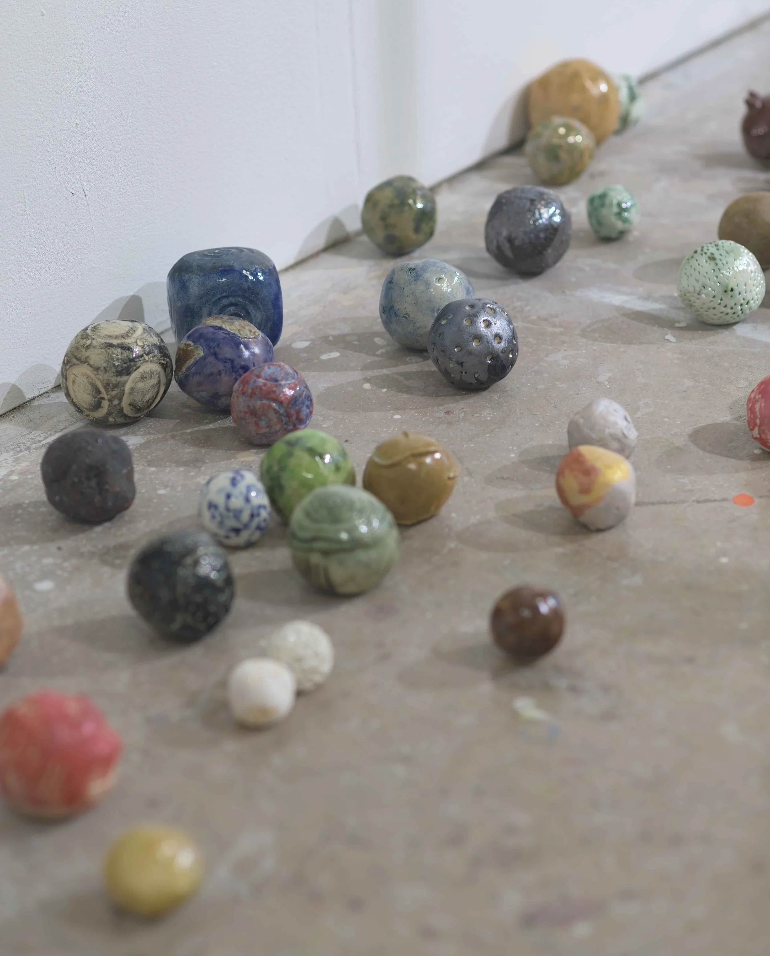 Multiple colorful ceramic or glass spheres arranged on a light-colored floor, against a white wall.