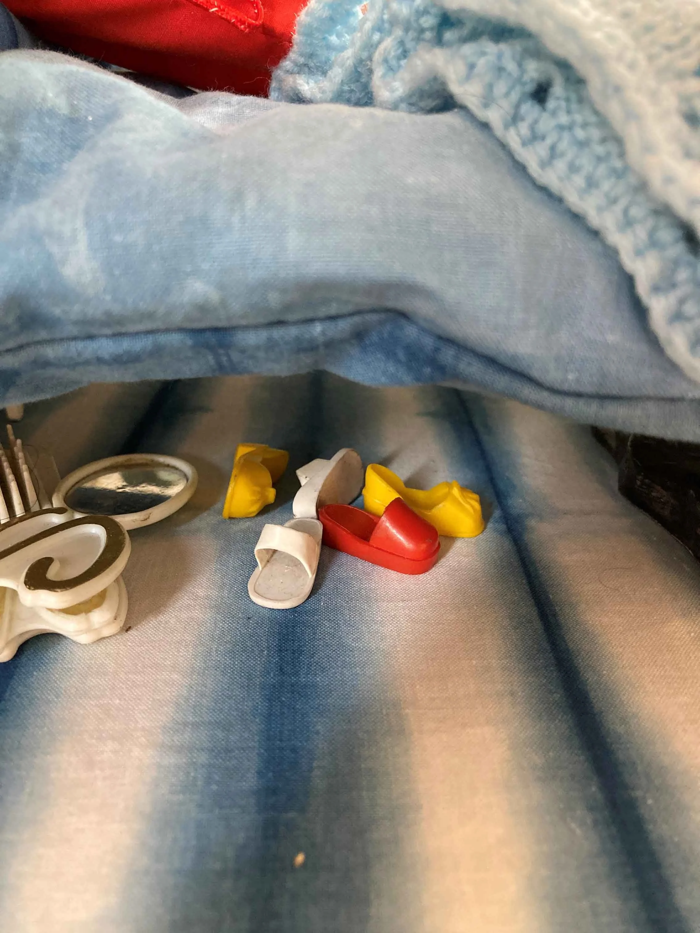 Close up of Sindy doll shoes on a blue fabric surface under a dolls bed.