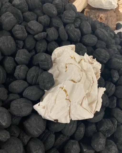 Crumpled white ceramic object, like paper, sitting on coal