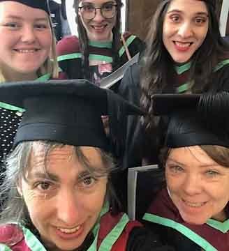 Group of five women, some wearing graduation caps and gowns, smiling together.