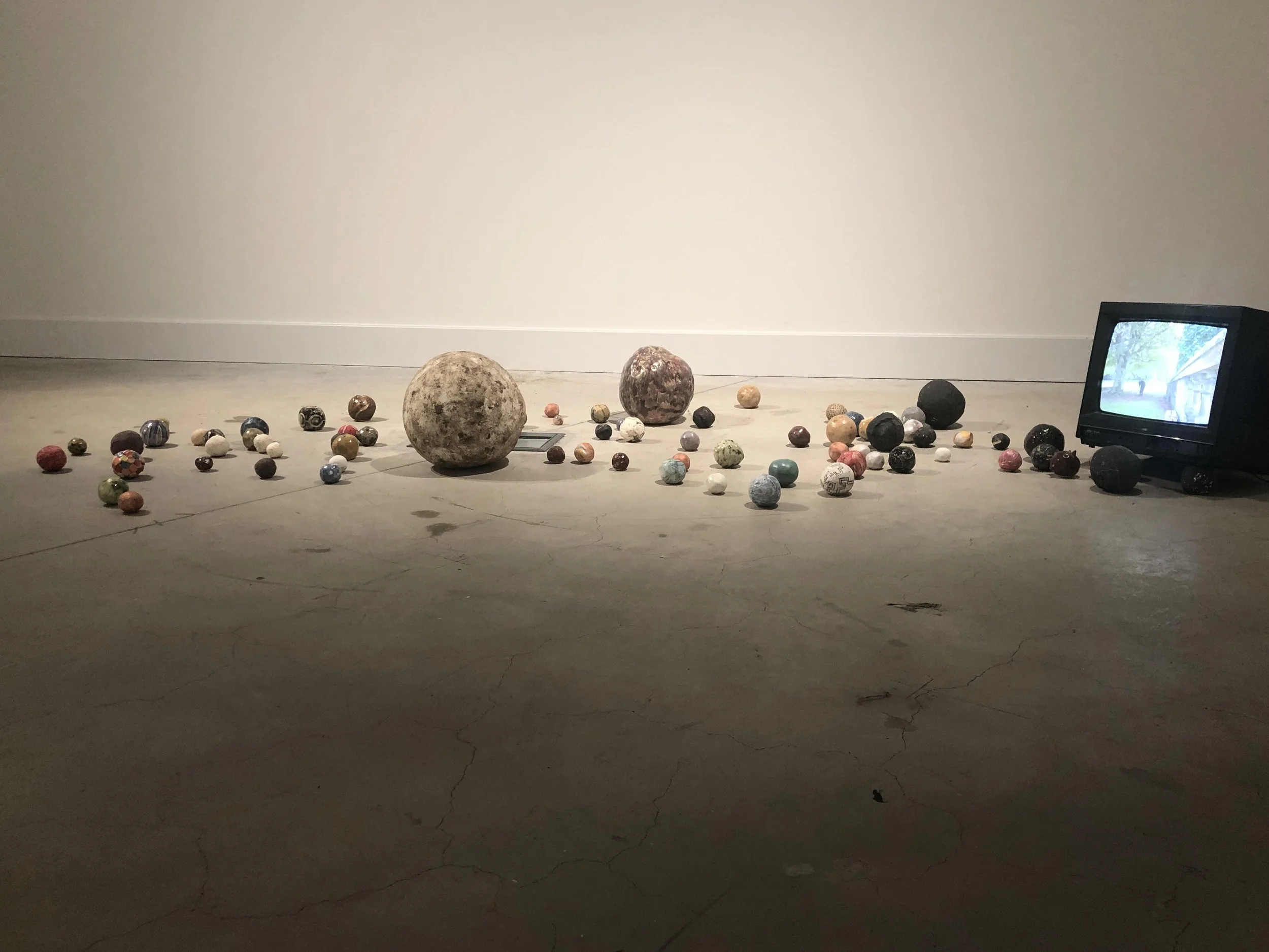 Various ceramic spheres arranged on a plain floor, with a small monitor on the right side showing a scene with trees and a building.