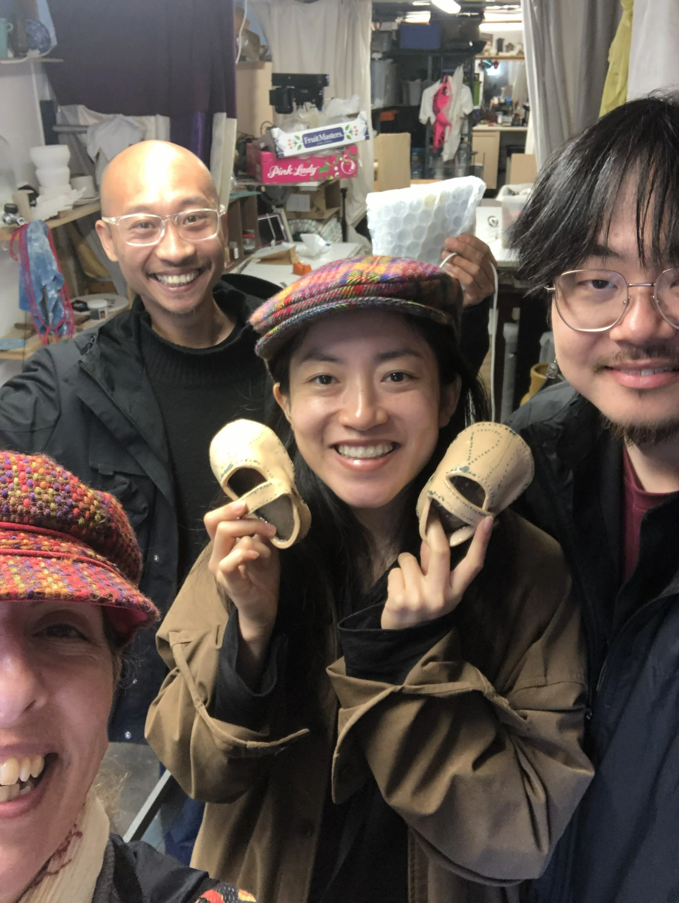 group of people standing in an art studio, one holds up ceramic childrens shoes