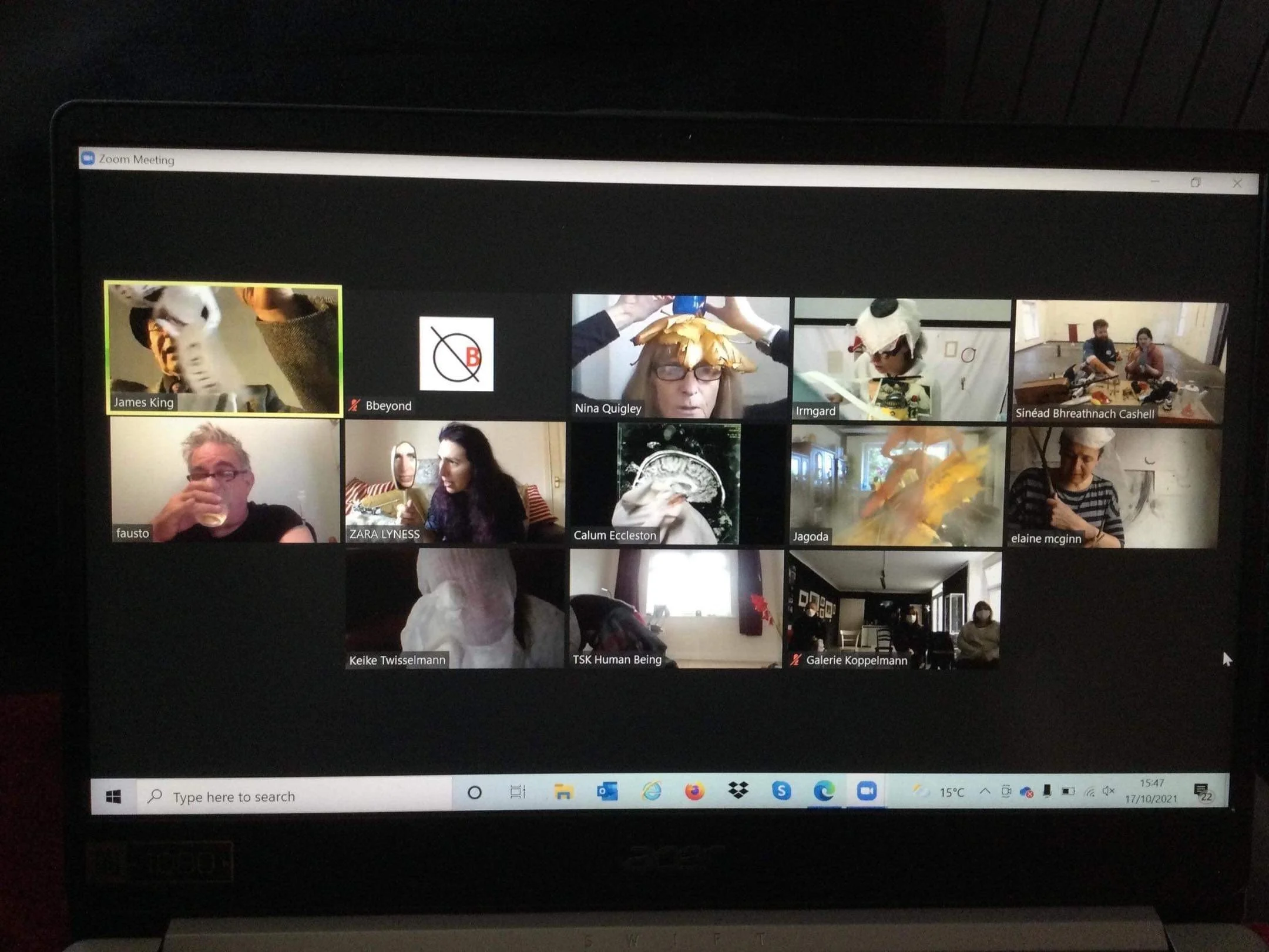 Screenshot of a Zoom video conference call with multiple participants, some wearing costumes or accessories, and a dark background.