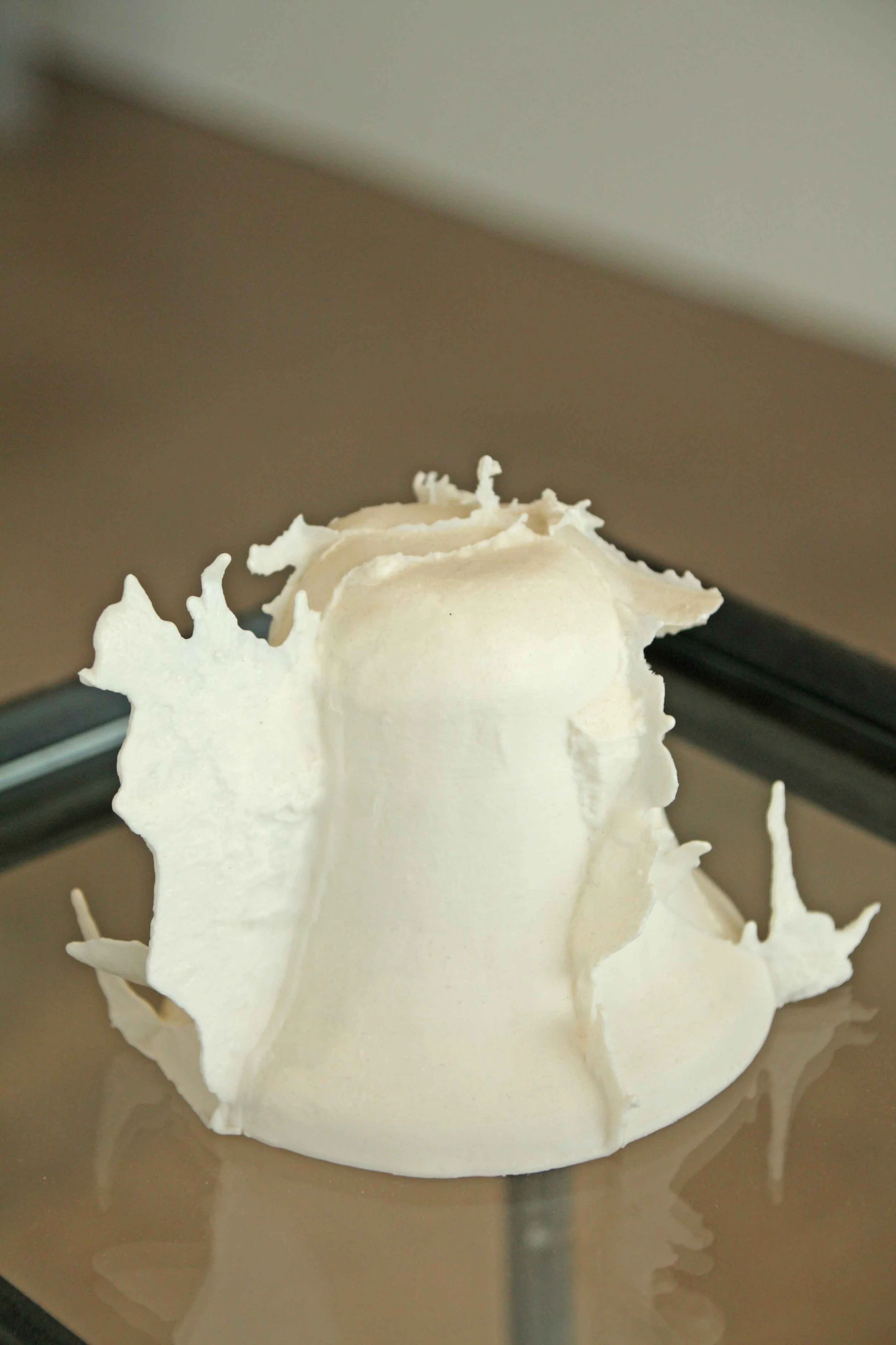 Close-up of a white bellsculpture with intricate, jagged edges, placed on a reflective surface.