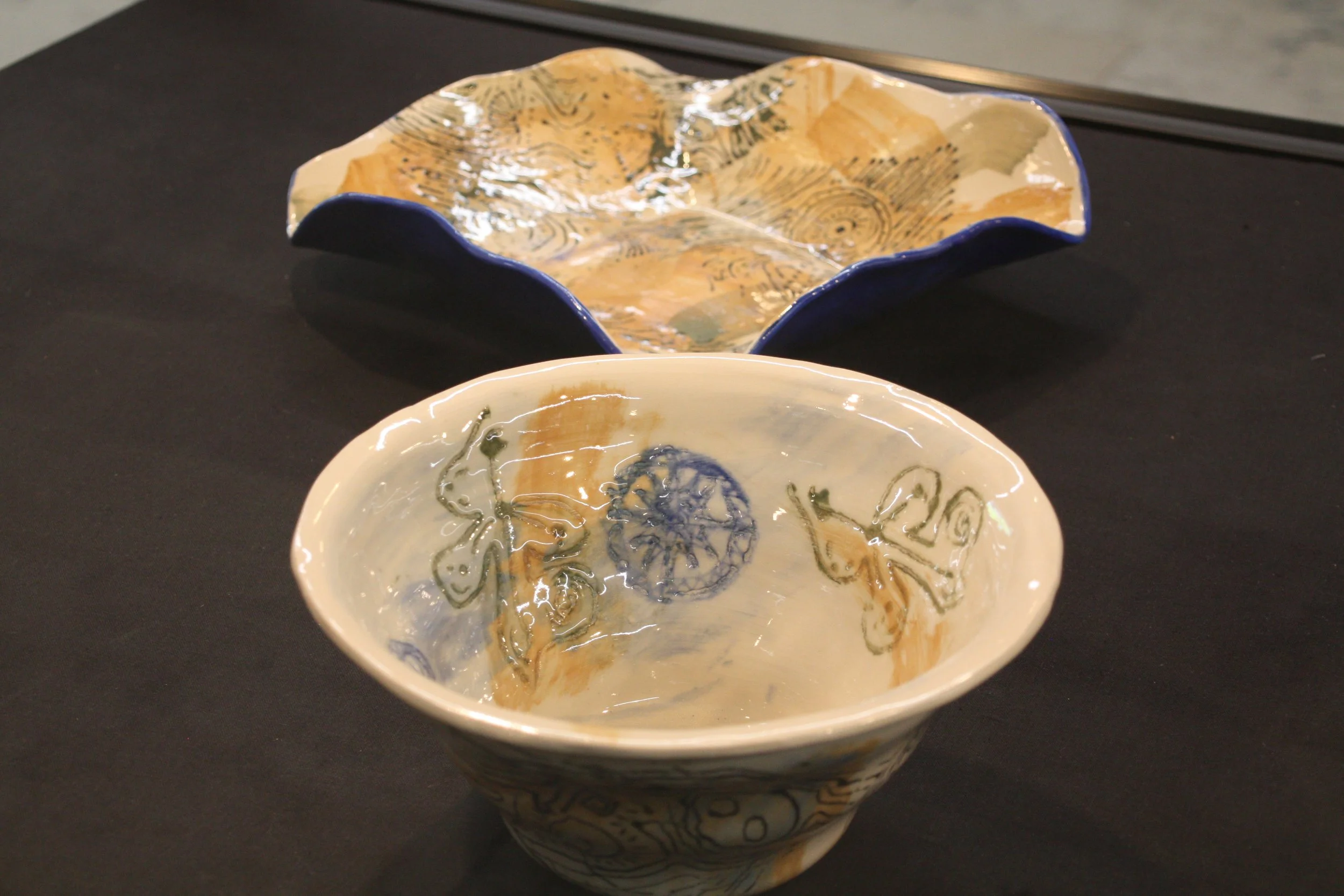 Two decorated ceramic bowls with abstract patterns, one in the foreground and the other in the background, placed on a black surface.
