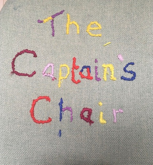 Colorful embroidery spelling out "The Captains Chair" on green  fabric