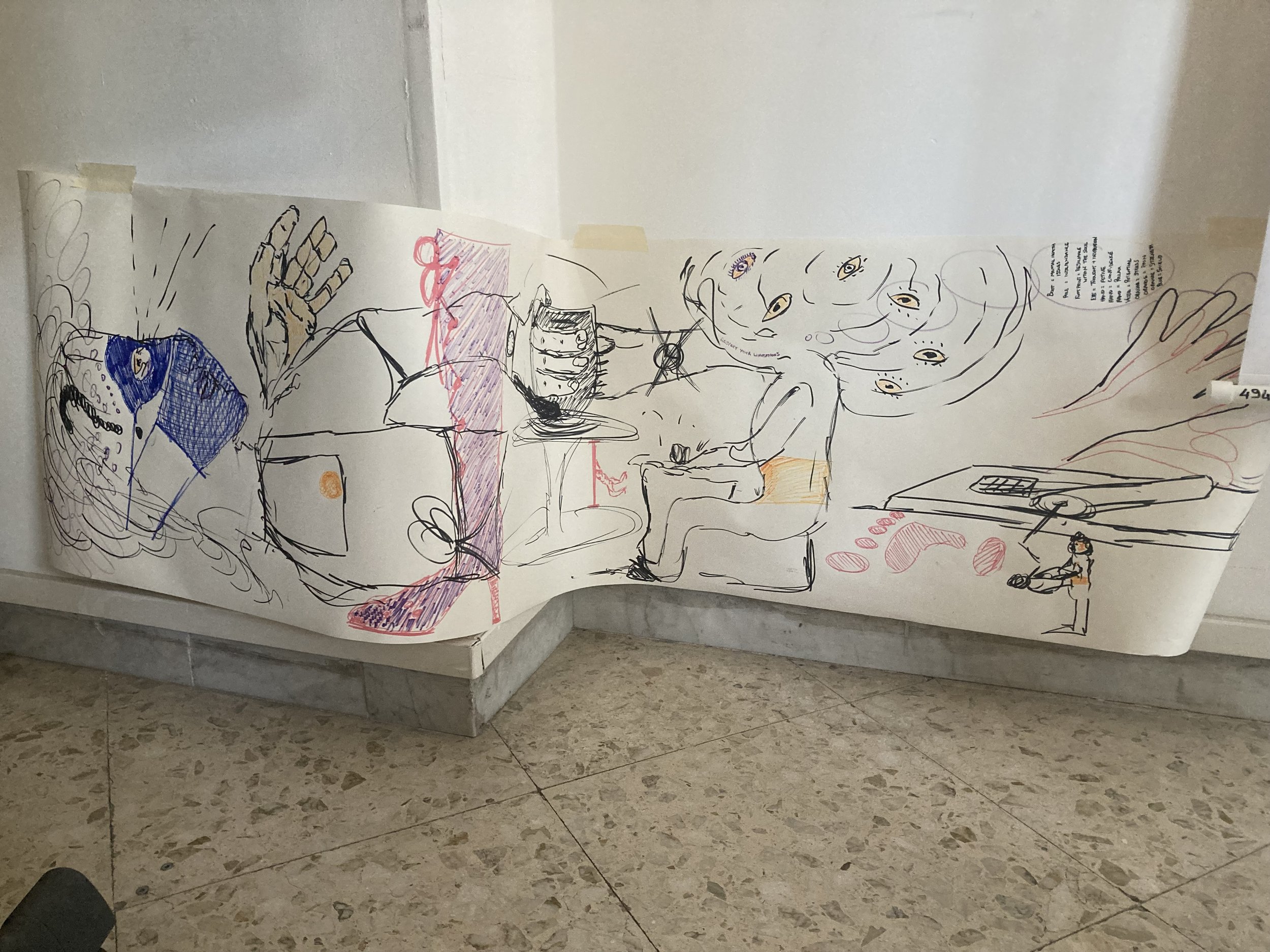 A wall with a large abstract drawing created with black, red, purple, blue, and orange marker or pen. The drawing features multiple human faces with eyes, a hand, and various shapes and lines, some of which are detailed and others more abstract.