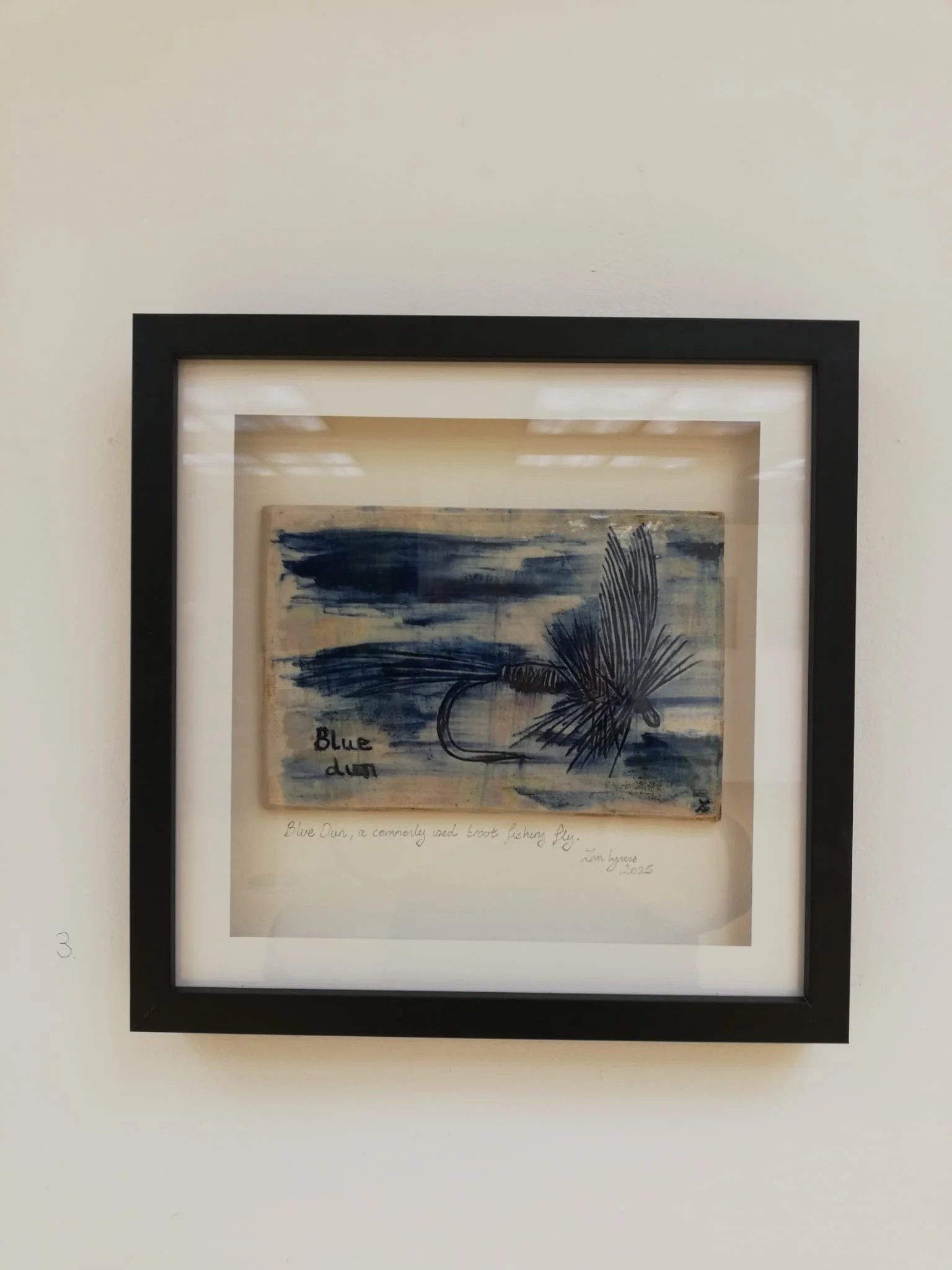 Framed ceramic tile of a blue fishing fly with handwritten notes, titled 'Blue Fly,' signed by the artist, 
