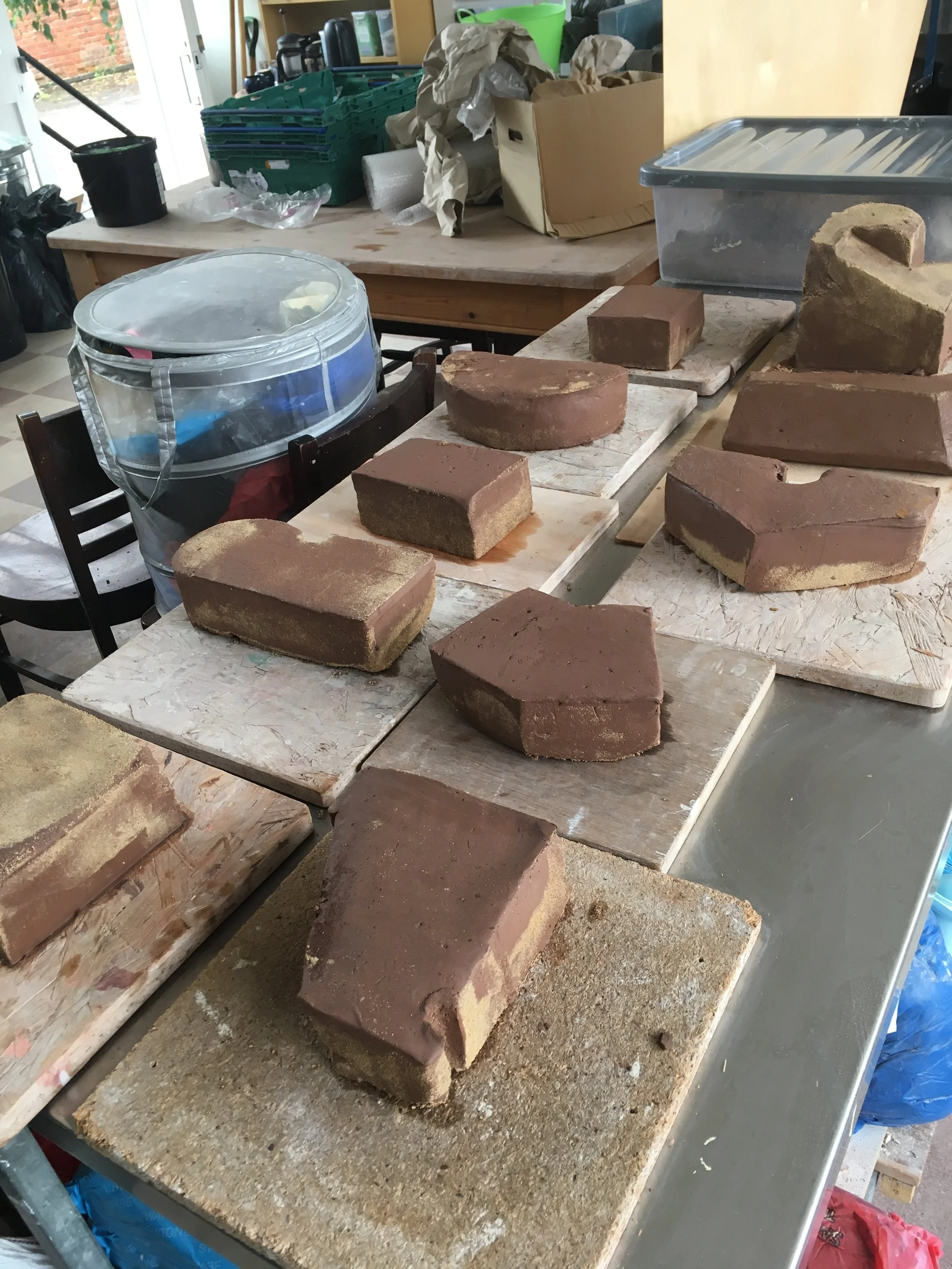 Several bricks of different shapes and sizes placed on wooden boards on a workshop table, with a cluttered background of various tools and supplies.