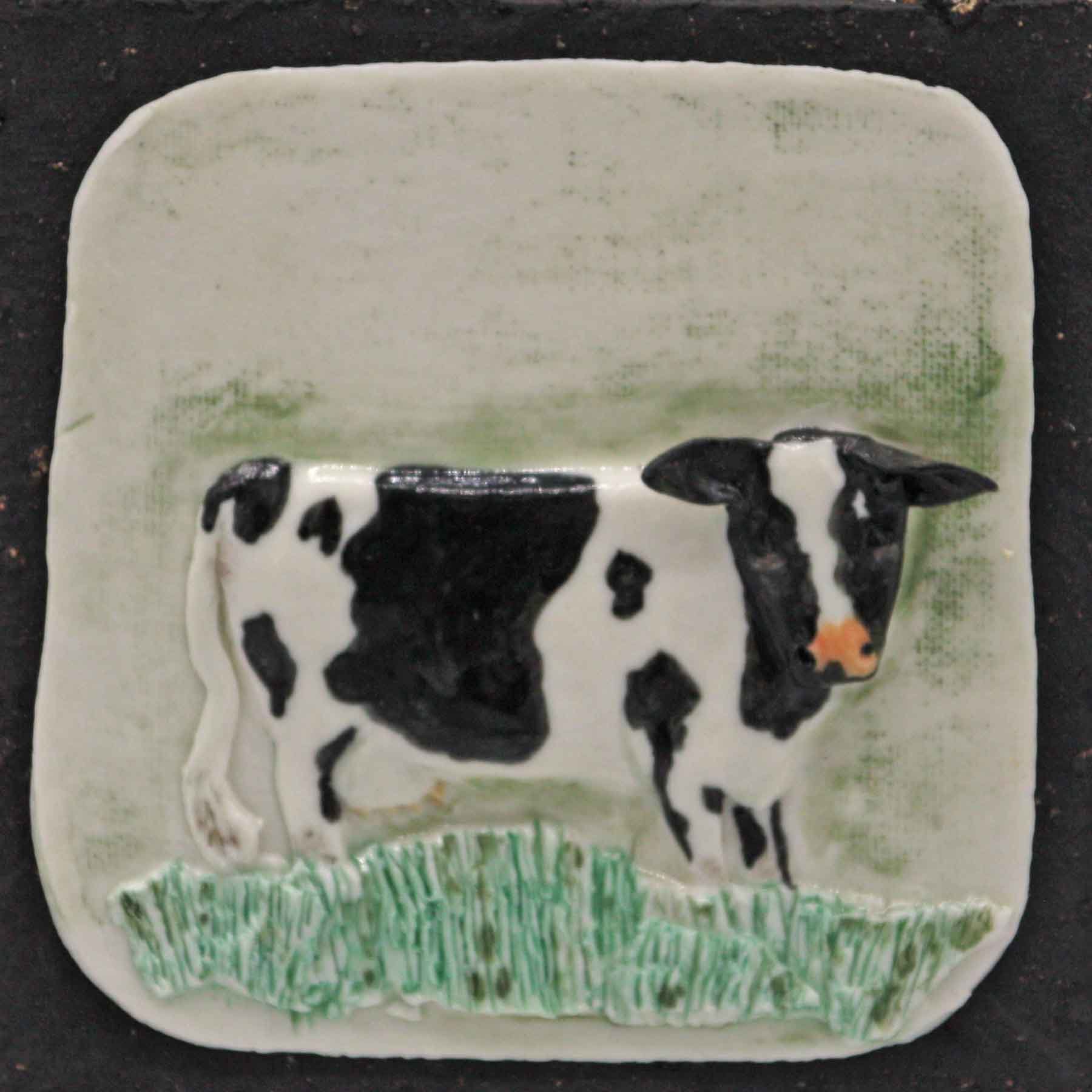Porcelain tile depicting a cow, decorated with black spots and an orange nose, on a green textured background.