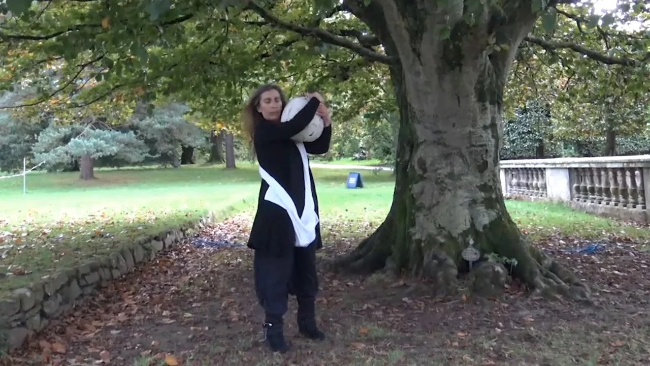 Woman hugging a white and black ceramic ball on a tree in a park.