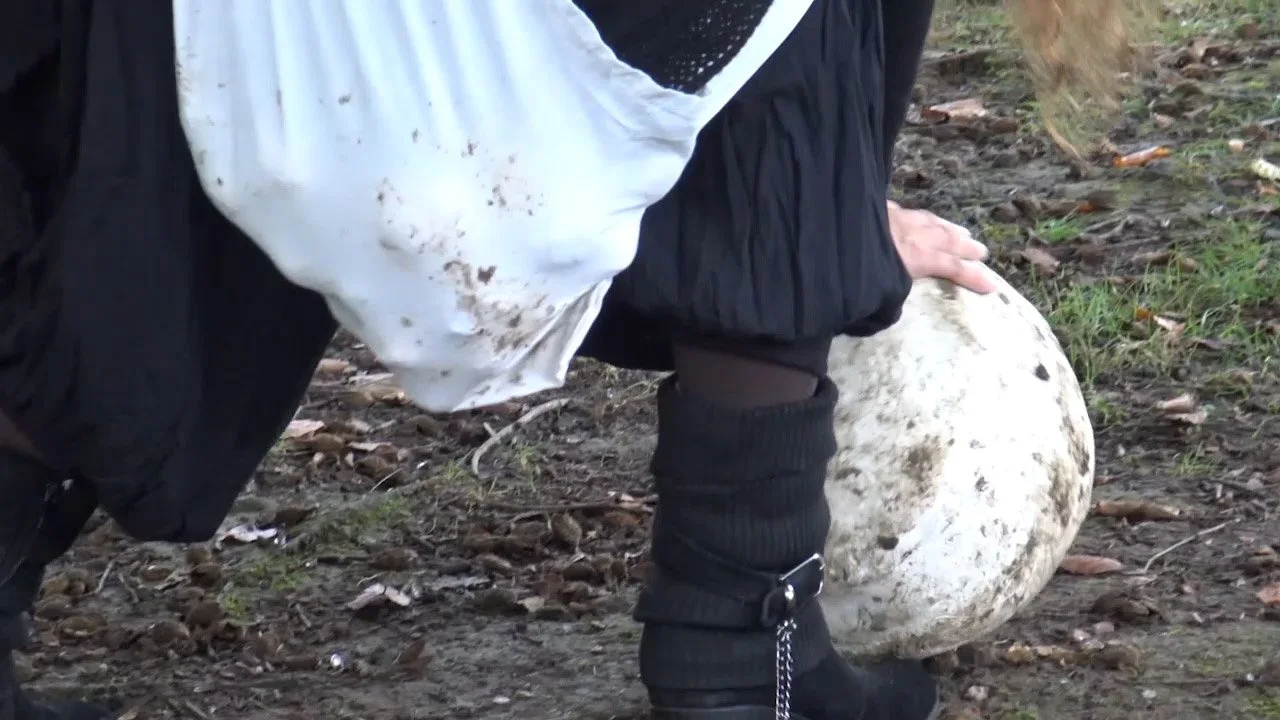 Person holding a large, rounded ceramic ball outdoors on dirt ground