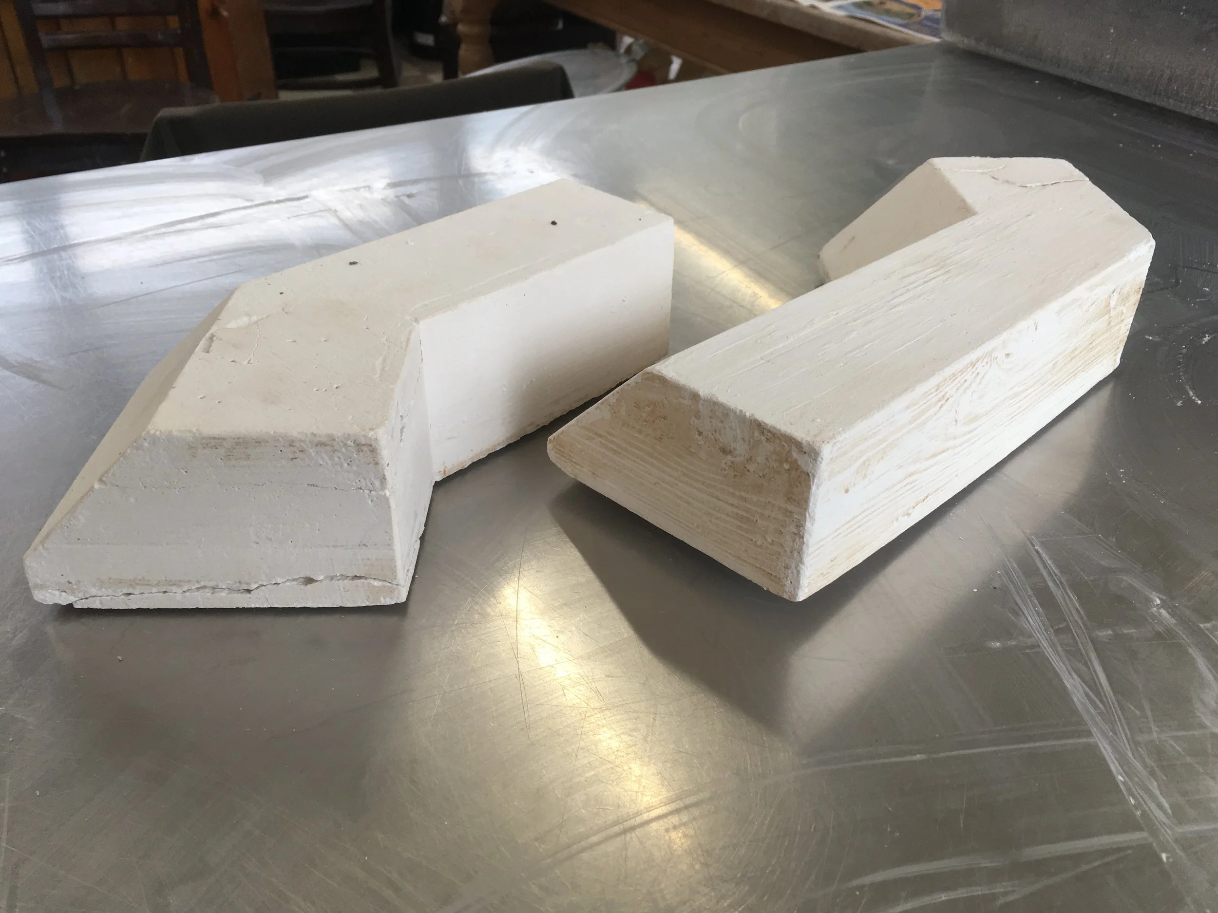 Two large white blocks of plaster with beveled edges on a metallic surface in a workshop.