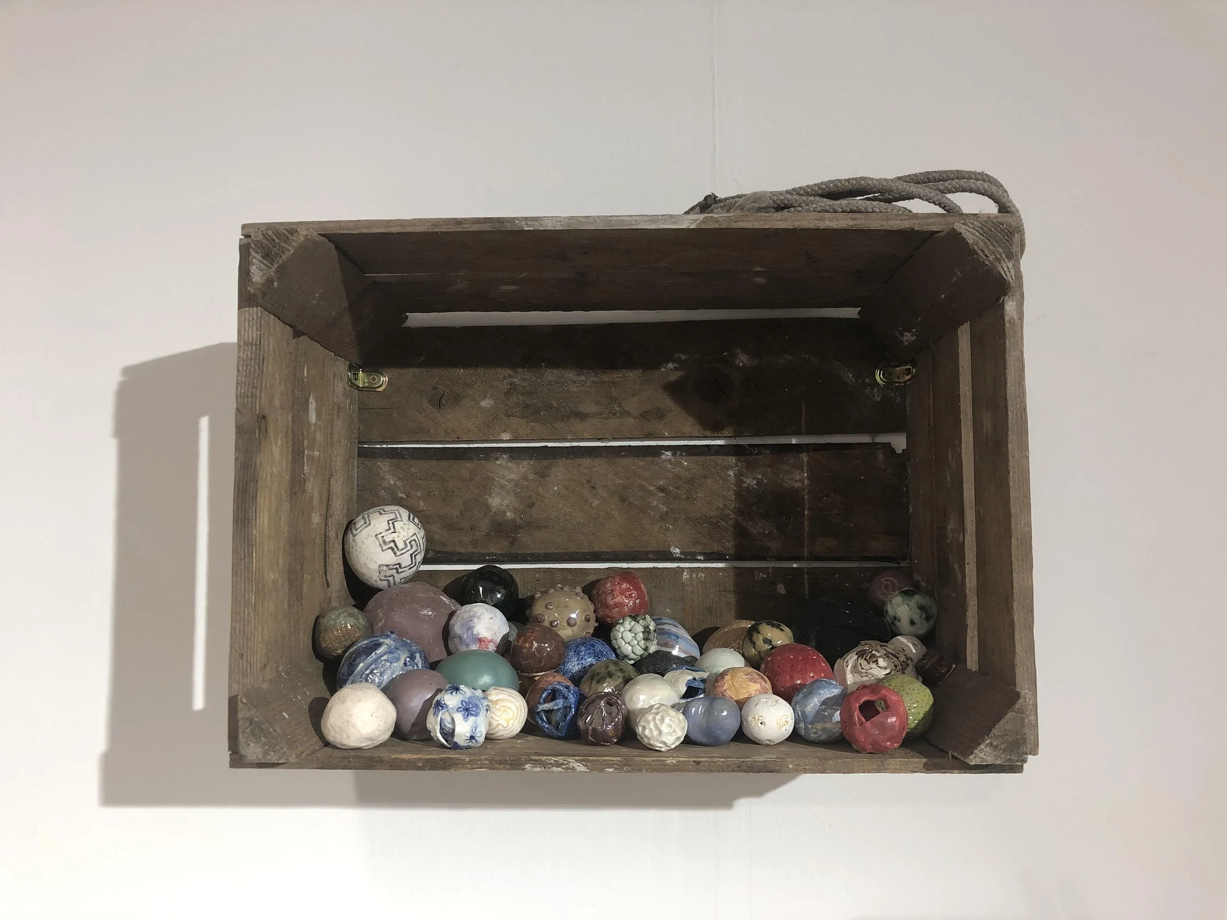 A wooden display shelf with a collection of colorful decorative balls, some with marbled and patterned designs, against a white wall.