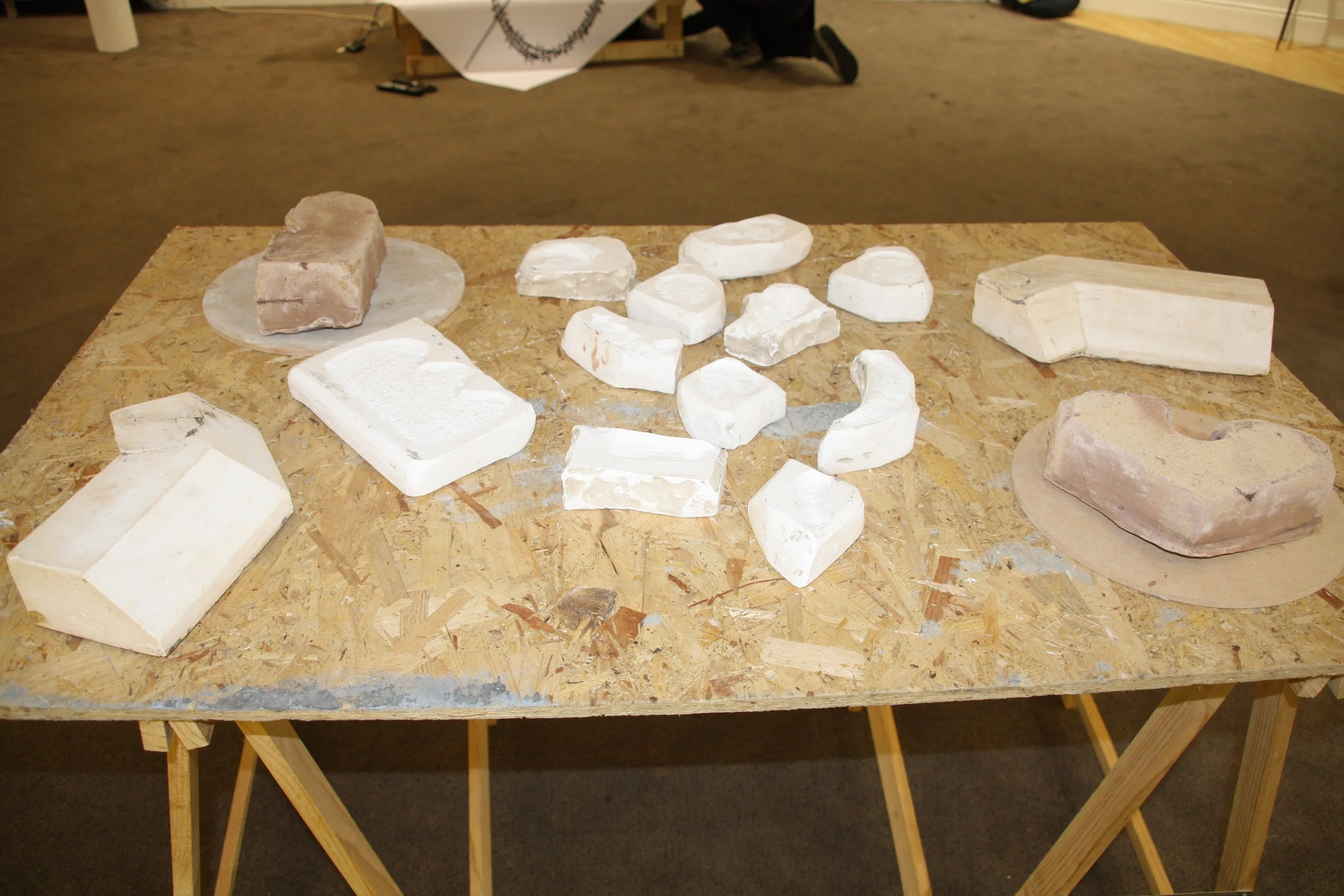 Various carved stone pieces arranged on a wooden table with a person working in the background.