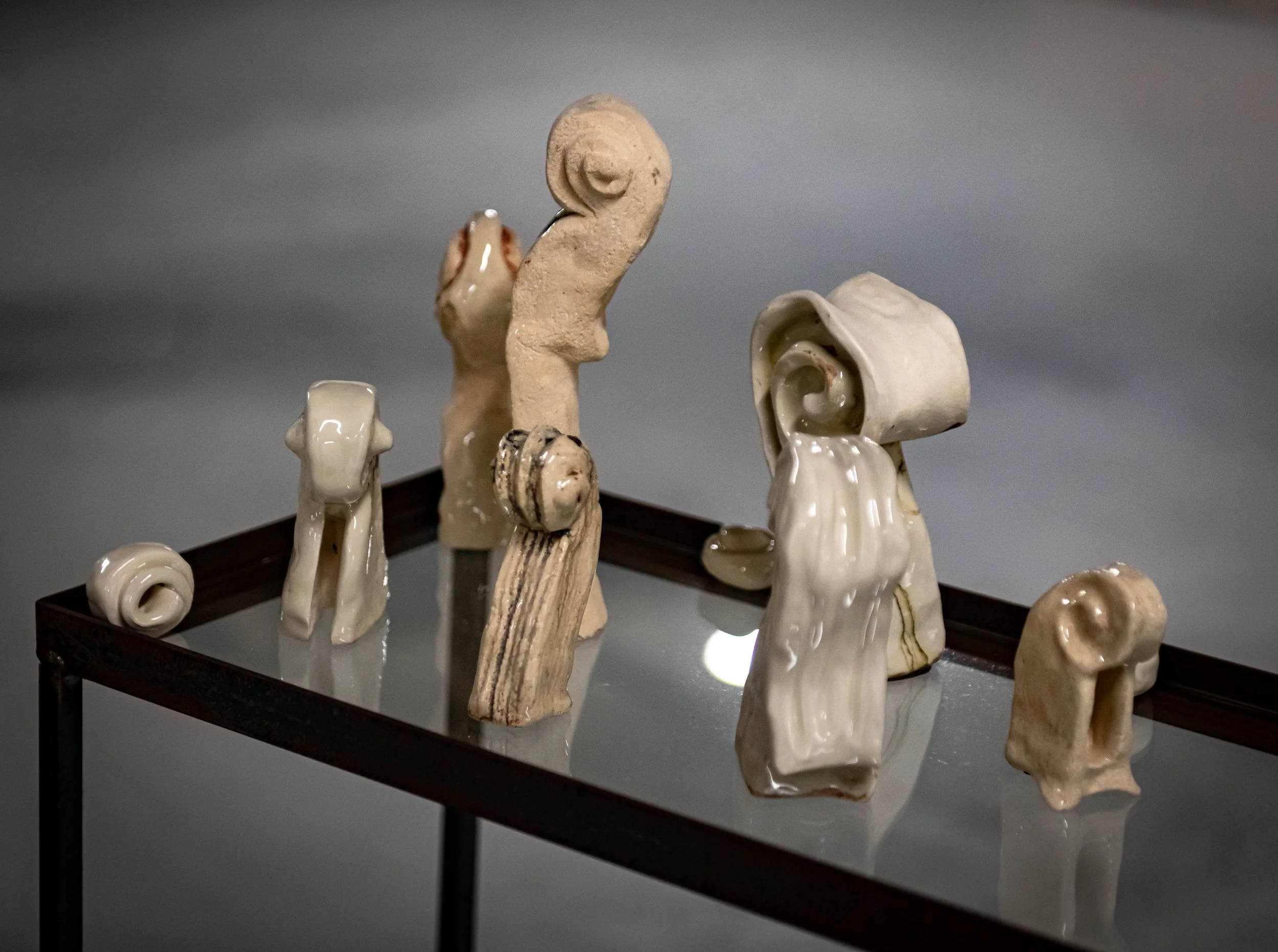 A collection of ceramic sculptures resembling violin scrolls displayed on a glass table against a gray background.