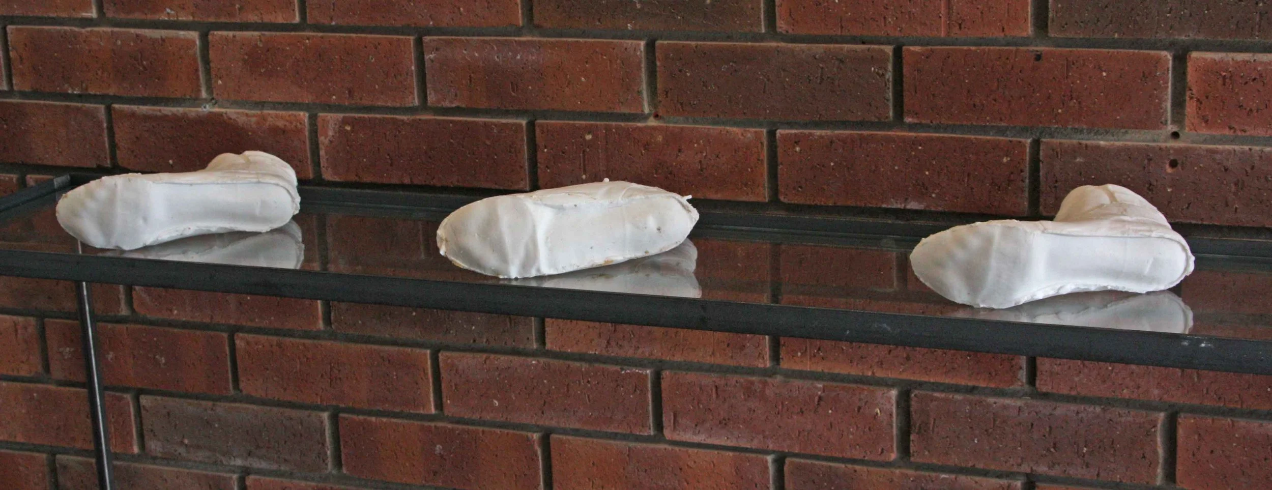 Three white, cast shoe interiors placed on a black glass shelf against a red brick wall.