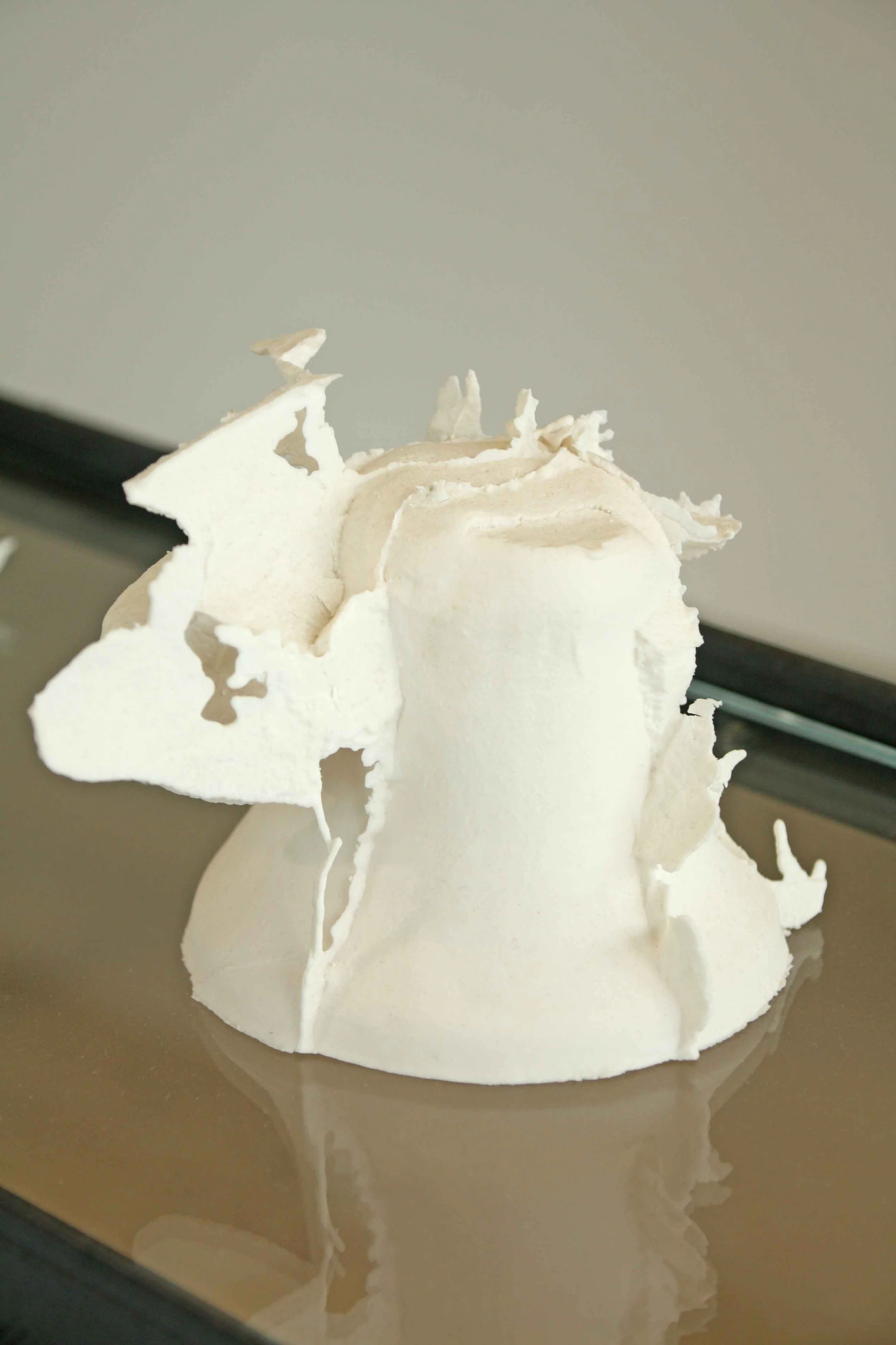 A white bell sculpture resembling a Christmas tree or winter scene, with intricate details, set on a reflective surface.