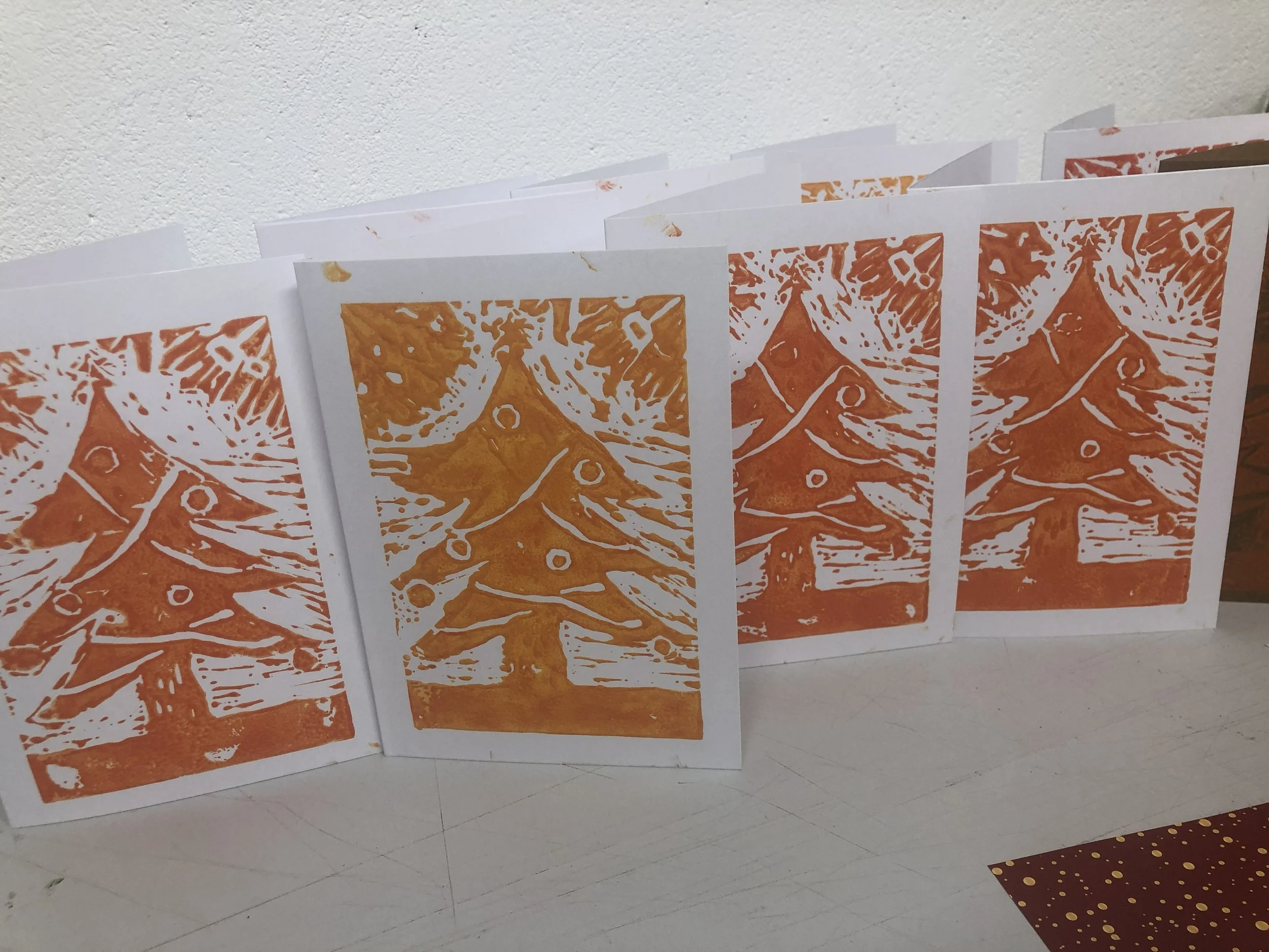 row of white christmas cards with orange christmas tree lino prints on the front