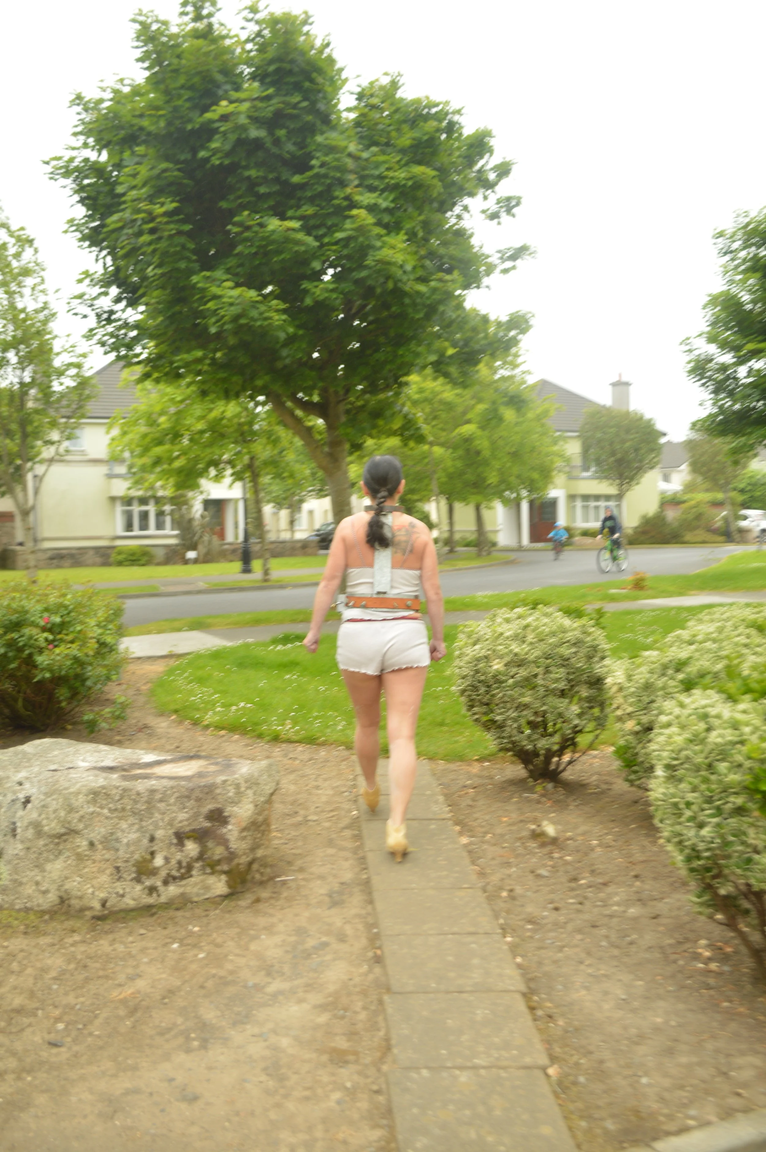 A woman walking on a sidewalk in a residential neighborhood with trees and houses in the background.