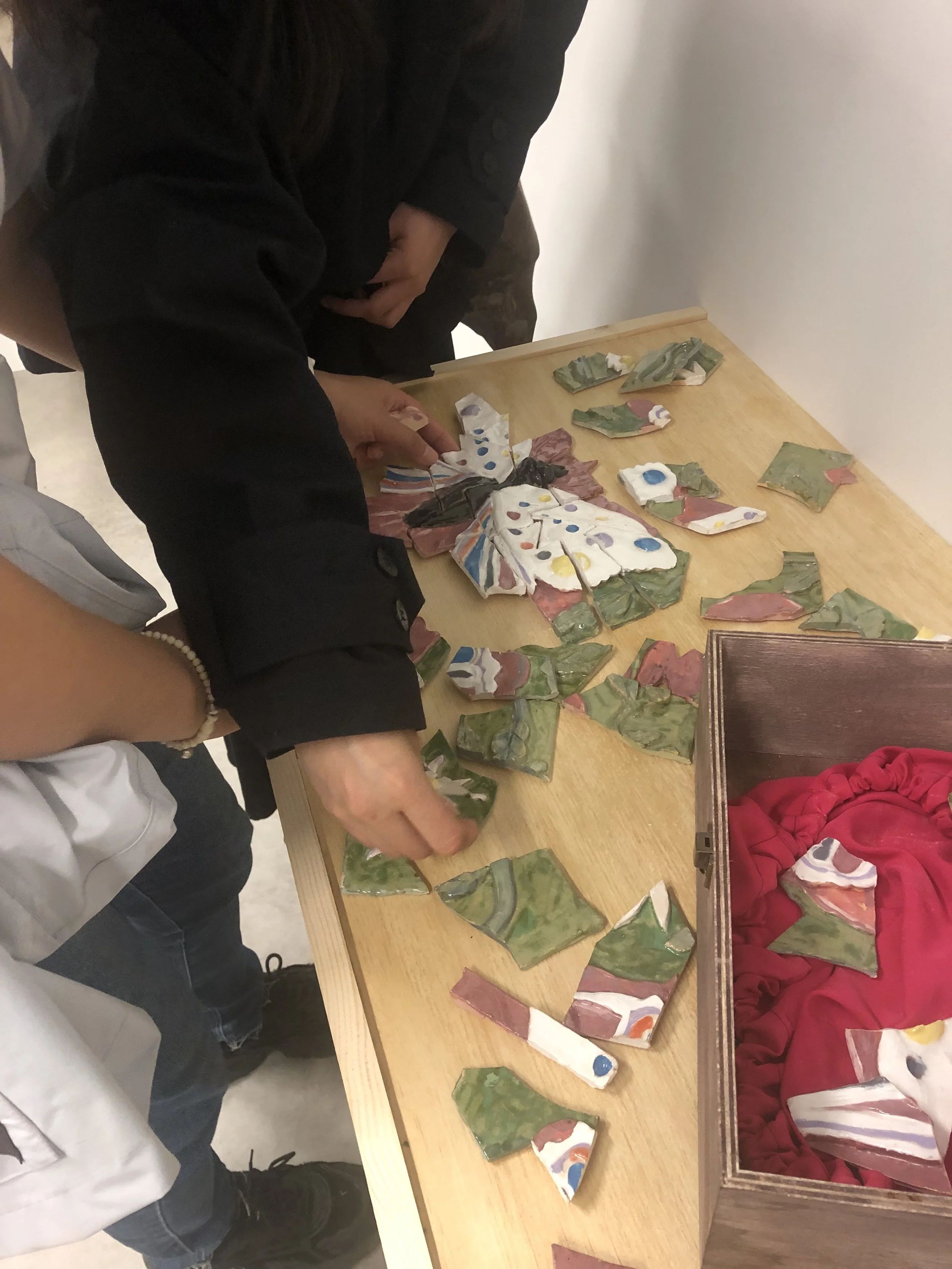 People working on assembling a mosaic of broken ceramic pieces on a wooden table.