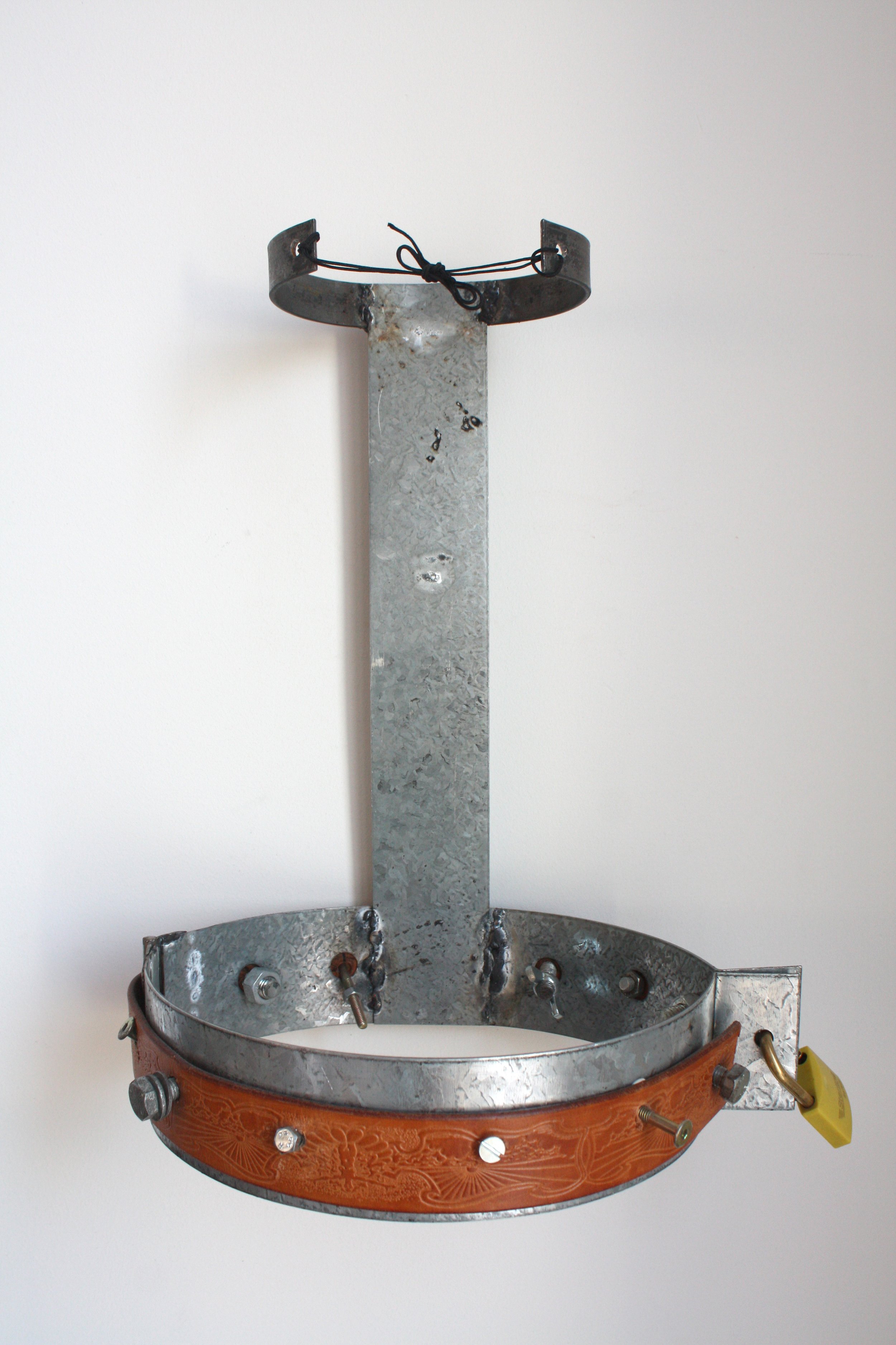 A metallic frame with a round, leather belt on the outer ring and internal components, including screws and metal bars, mounted on a plain white wall.