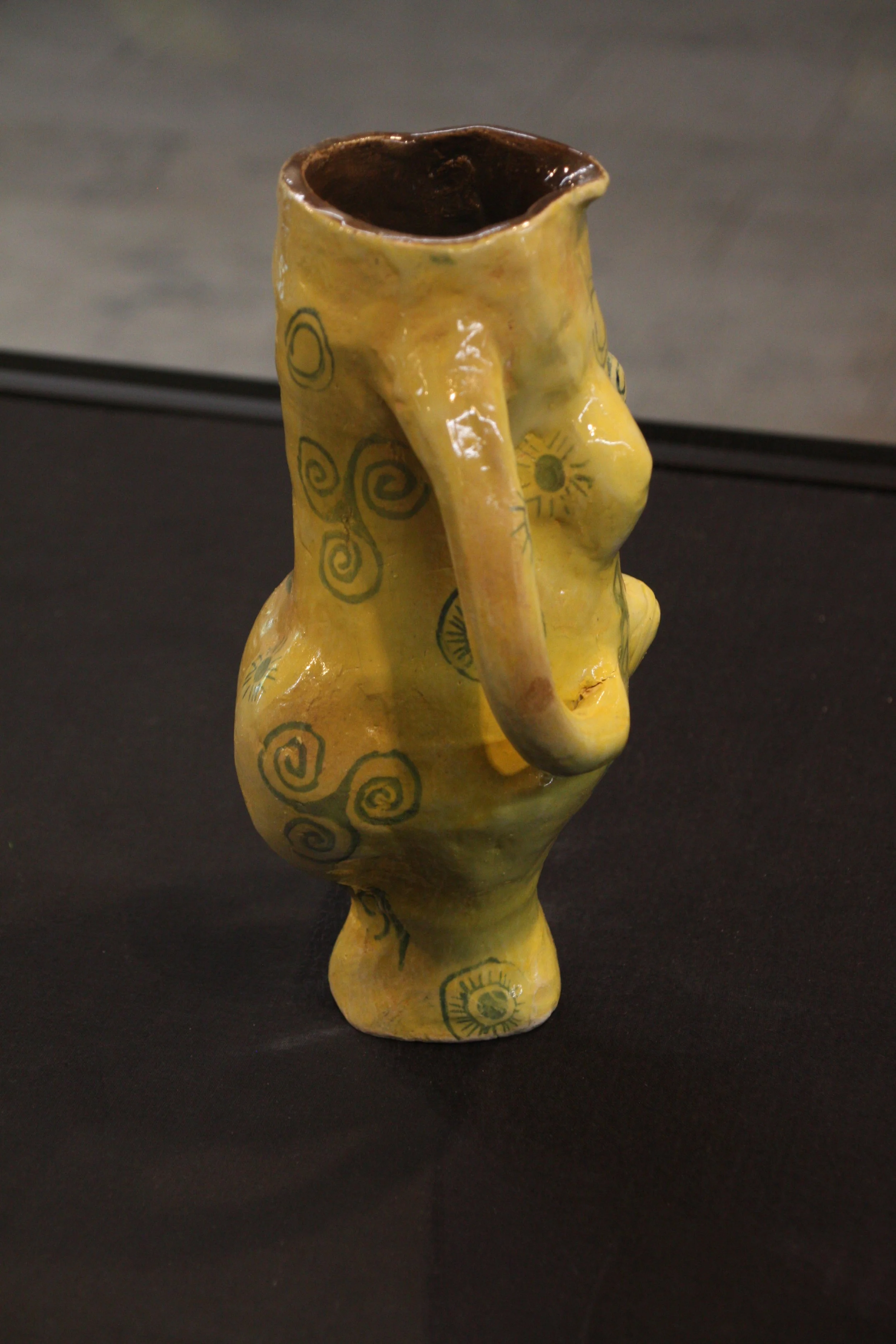 Yellow ceramic abstract female figure with blue spiral and sun designs on a black surface.