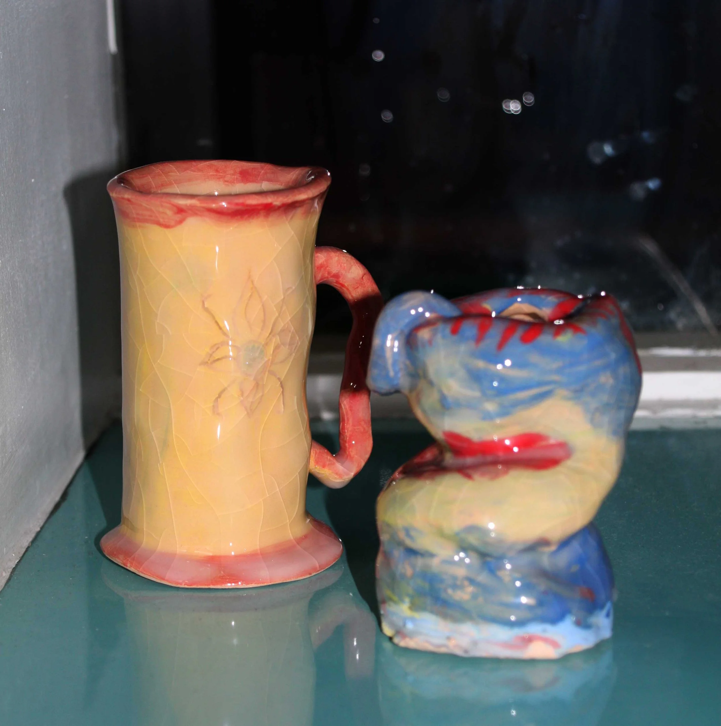Close-up of a multicolored ceramic mug with a handle, placed on a reflective surface with a dark background.