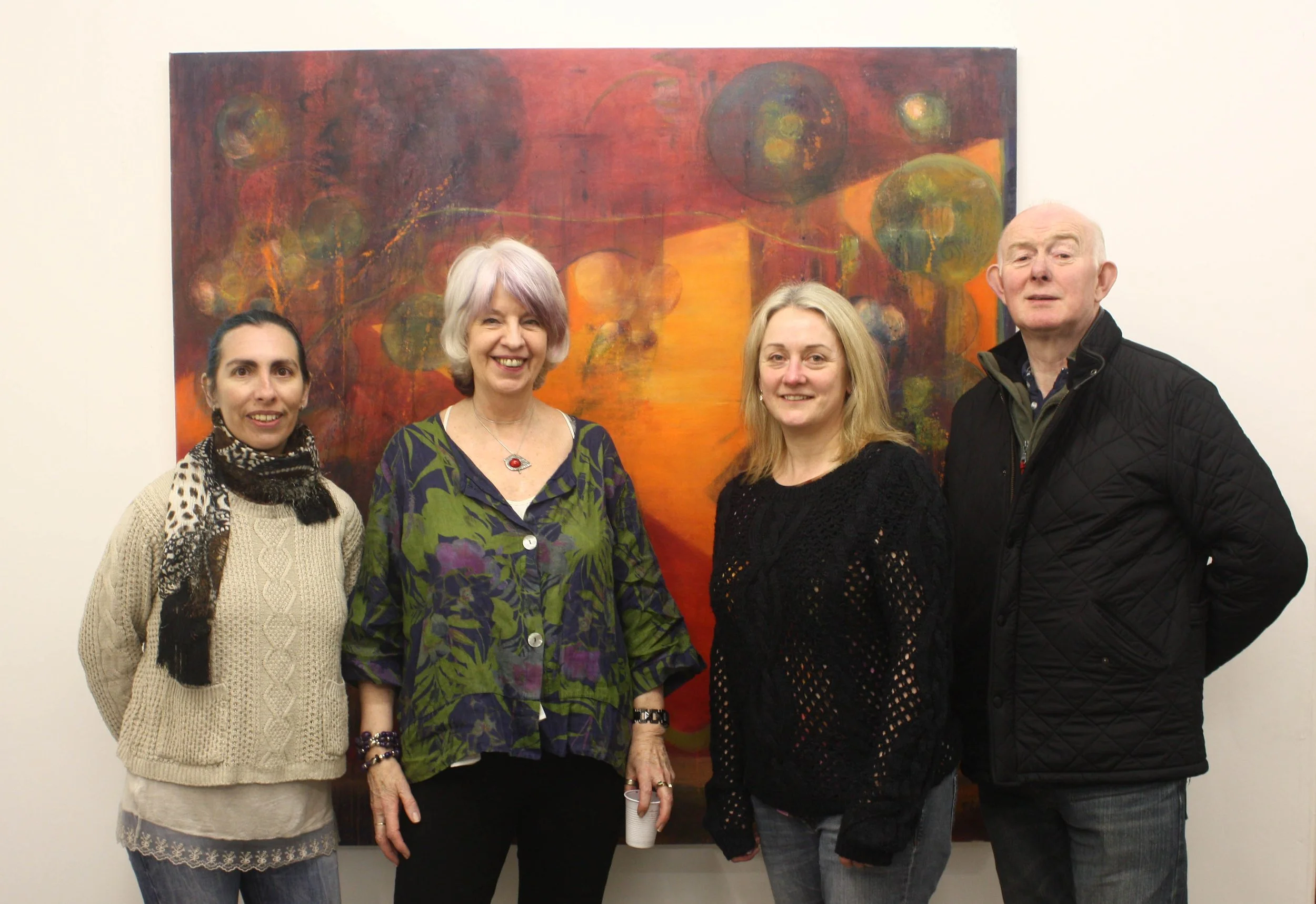 Four people standing in front of an abstract orange and red painting, smiling at the camera.