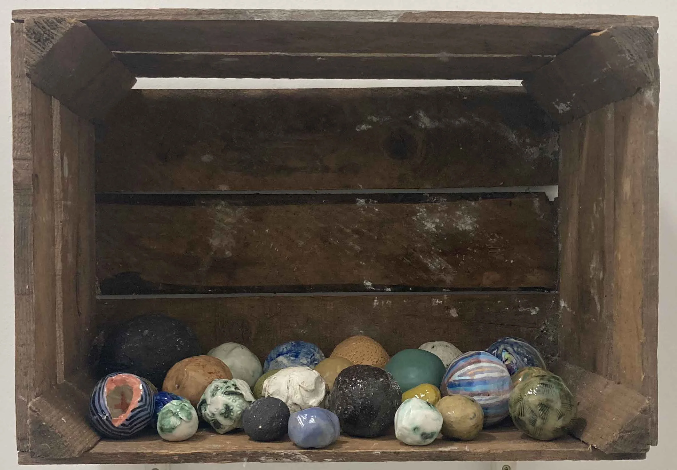 A wooden box filled with a variety of ceramic balls of different colors, patterns, and sizes.